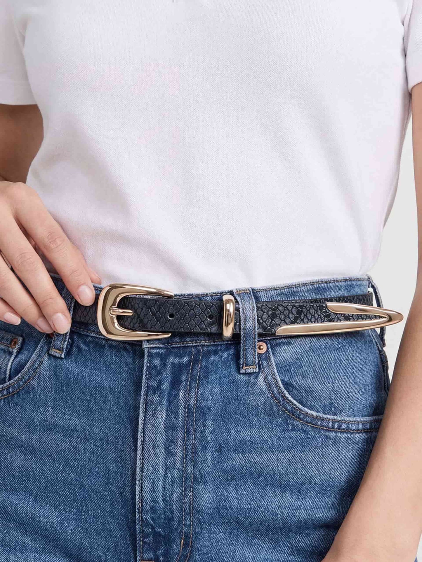 Model wearing grey suede belt with gold buckle styled with white shirt and blue jeans.