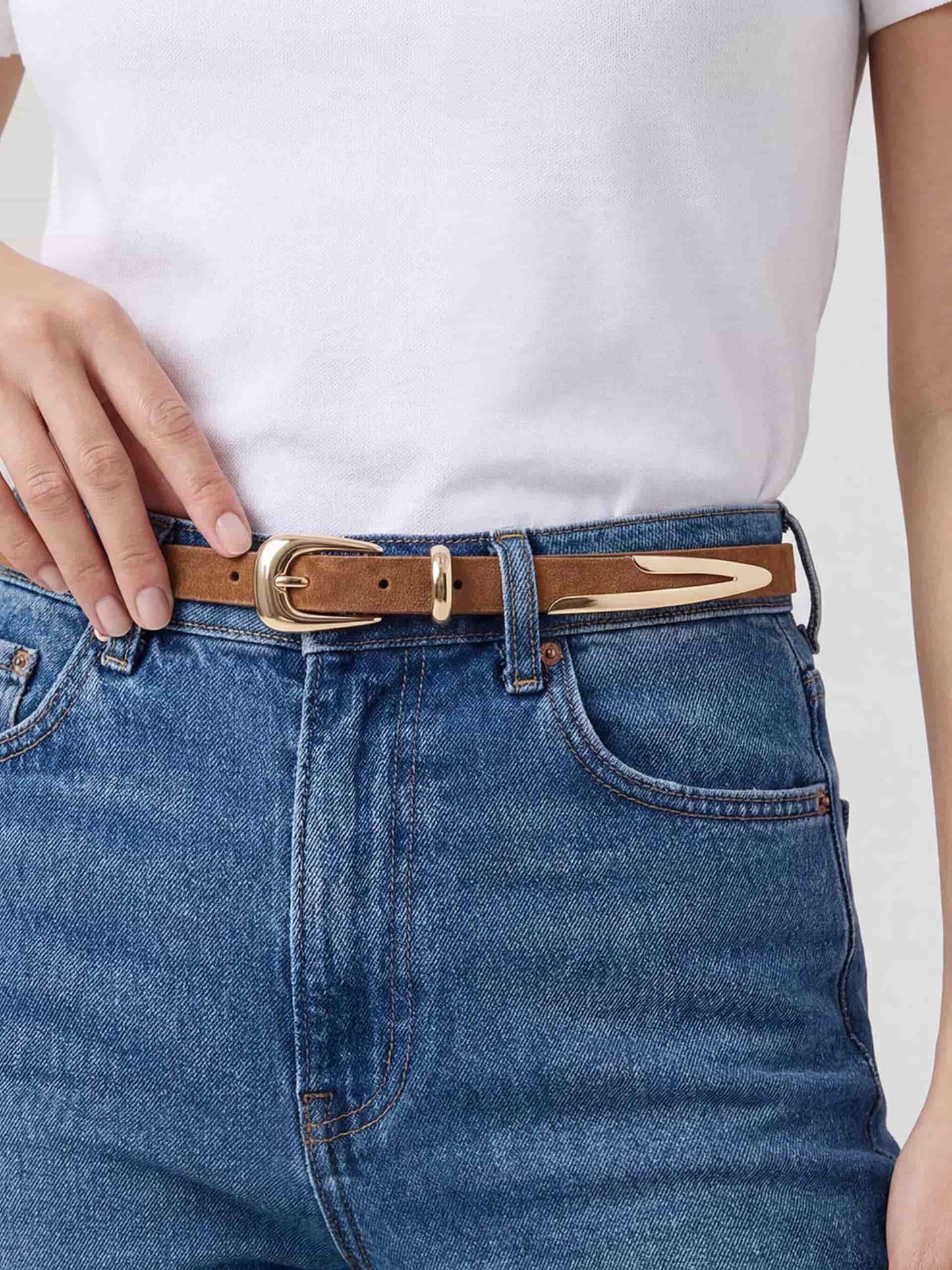 Model wearing brown leather belt with gold buckle, paired with white tee and denim jeans.