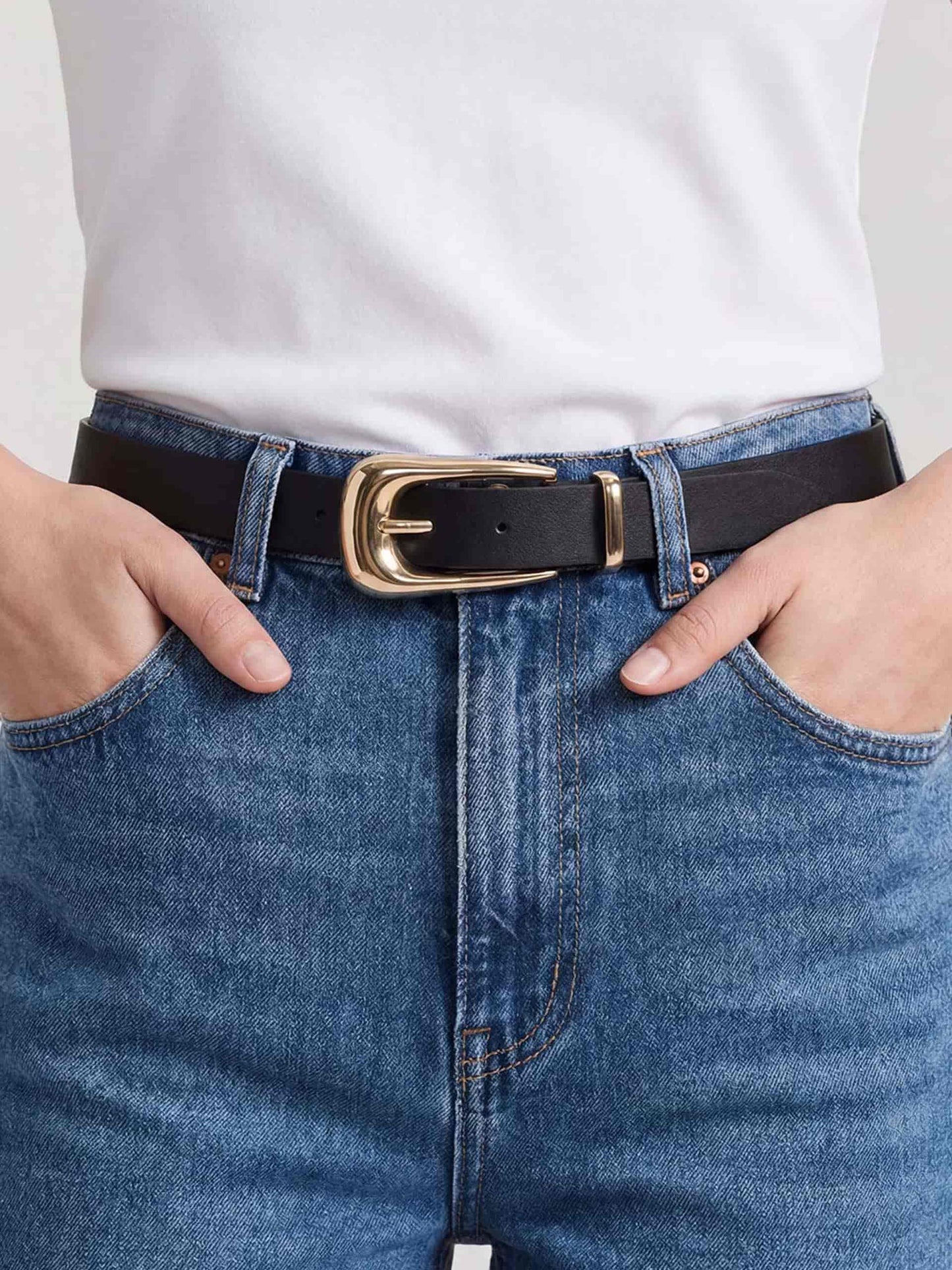 Close-up of black leather belt with gold buckle, worn with white shirt and blue jeans.