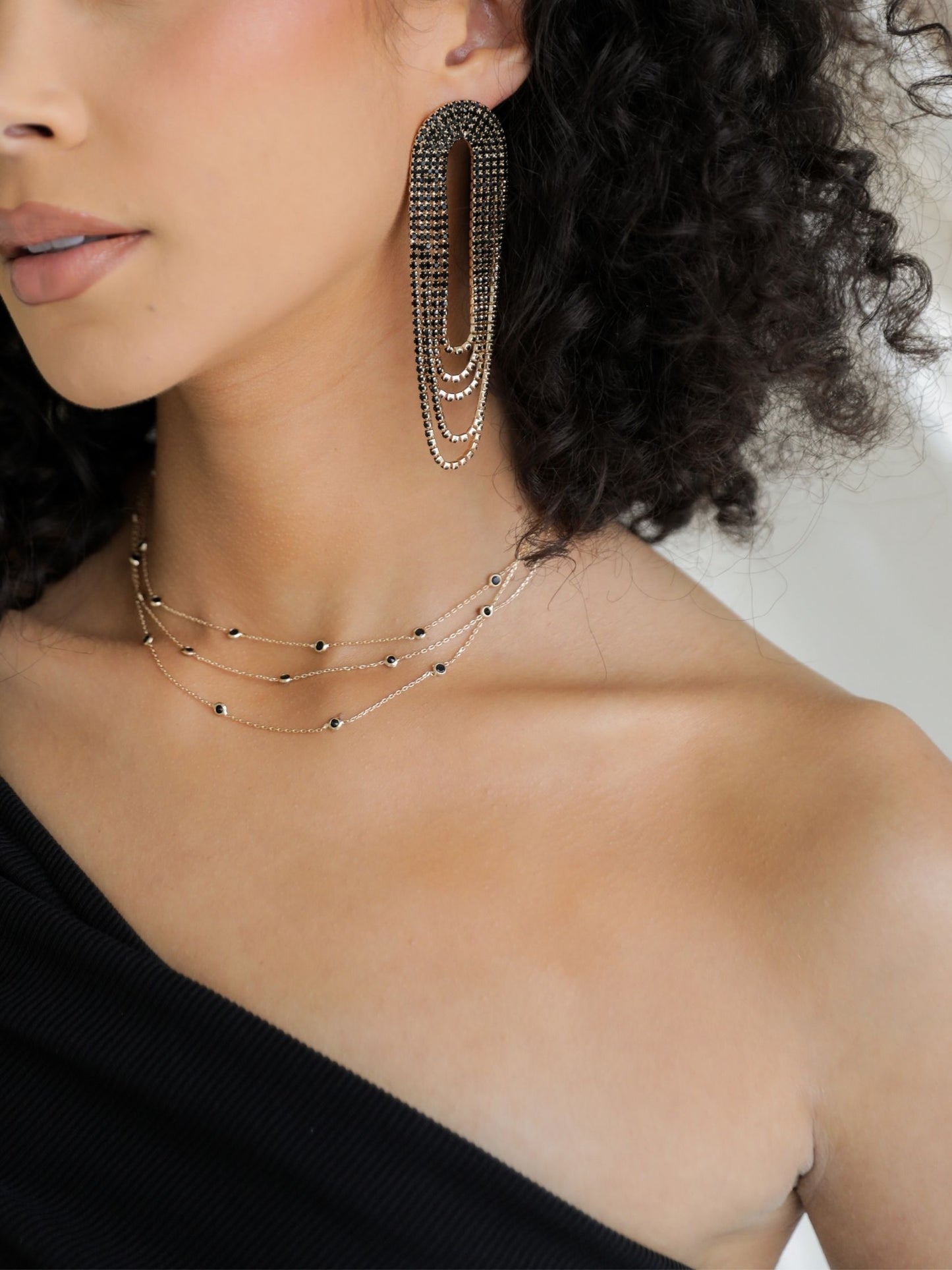 Close-up of a woman wearing gold hoop earrings and necklaces against a neutral background