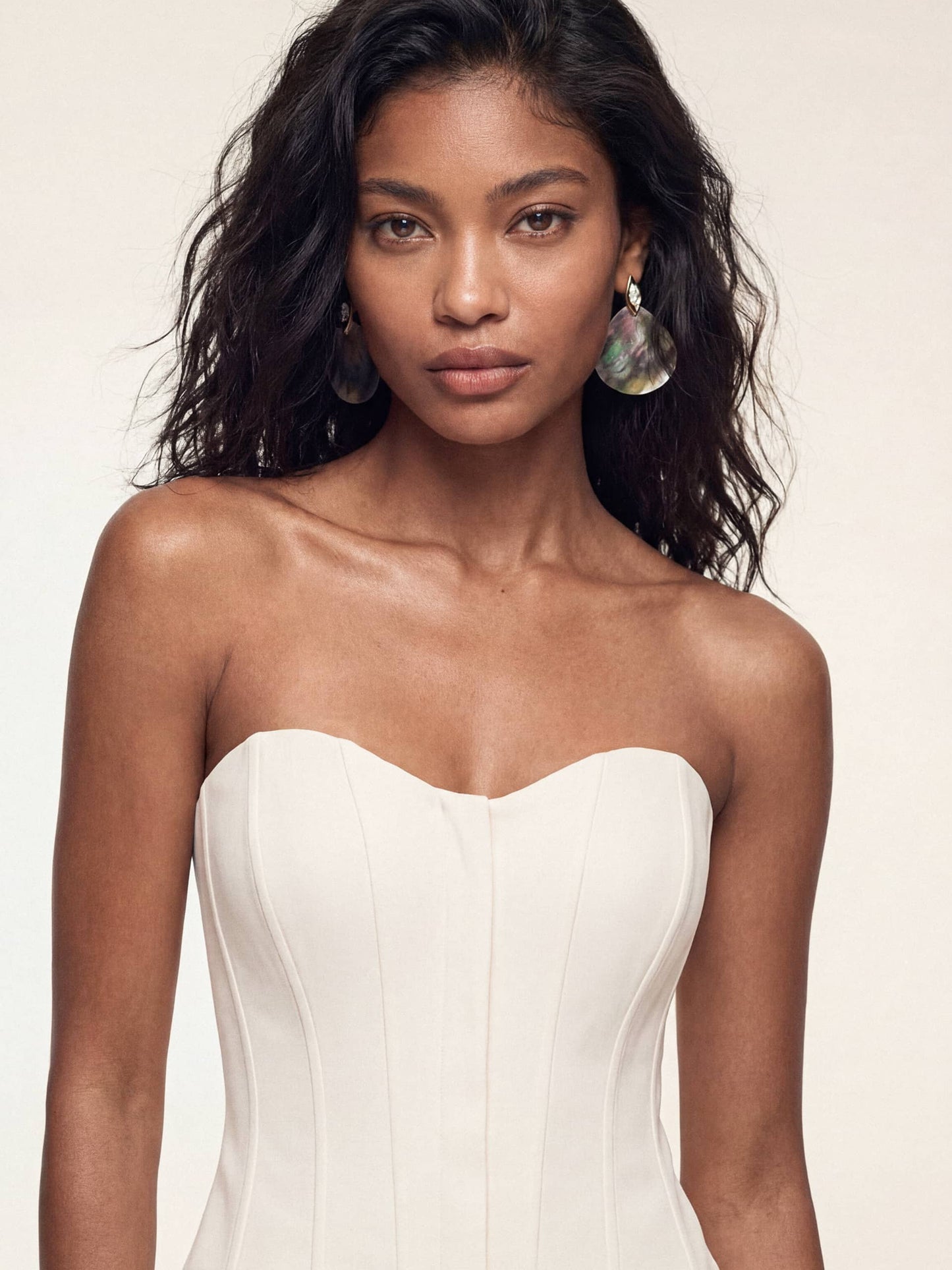 A woman wearing corset-style white dress with large, iridescent Shell Statement Earrings.