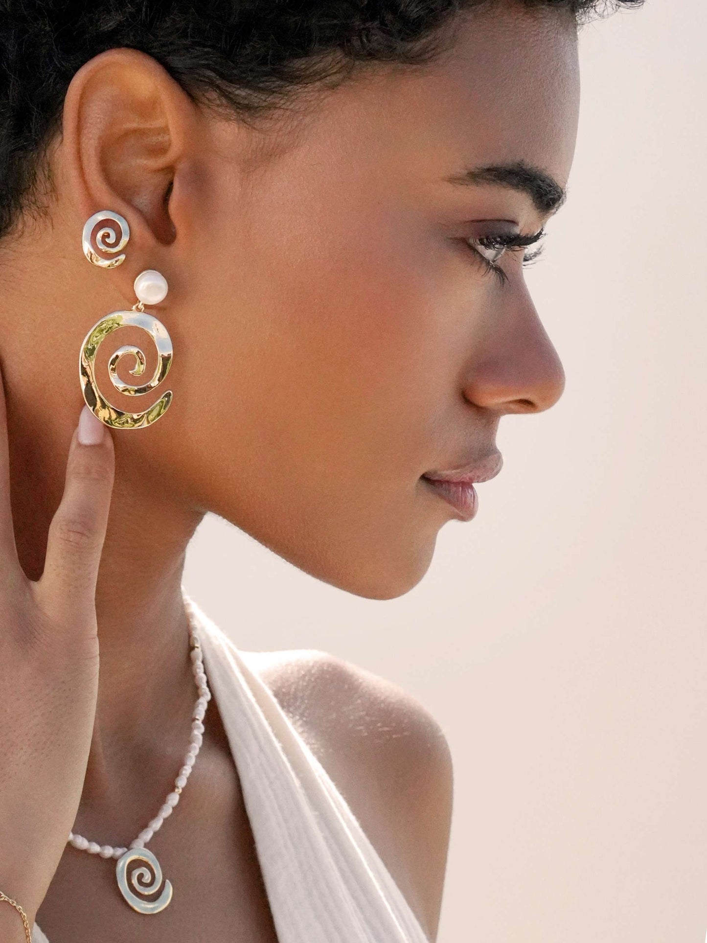 Close-up of a woman wearing spiral earrings and a necklace against a neutral background