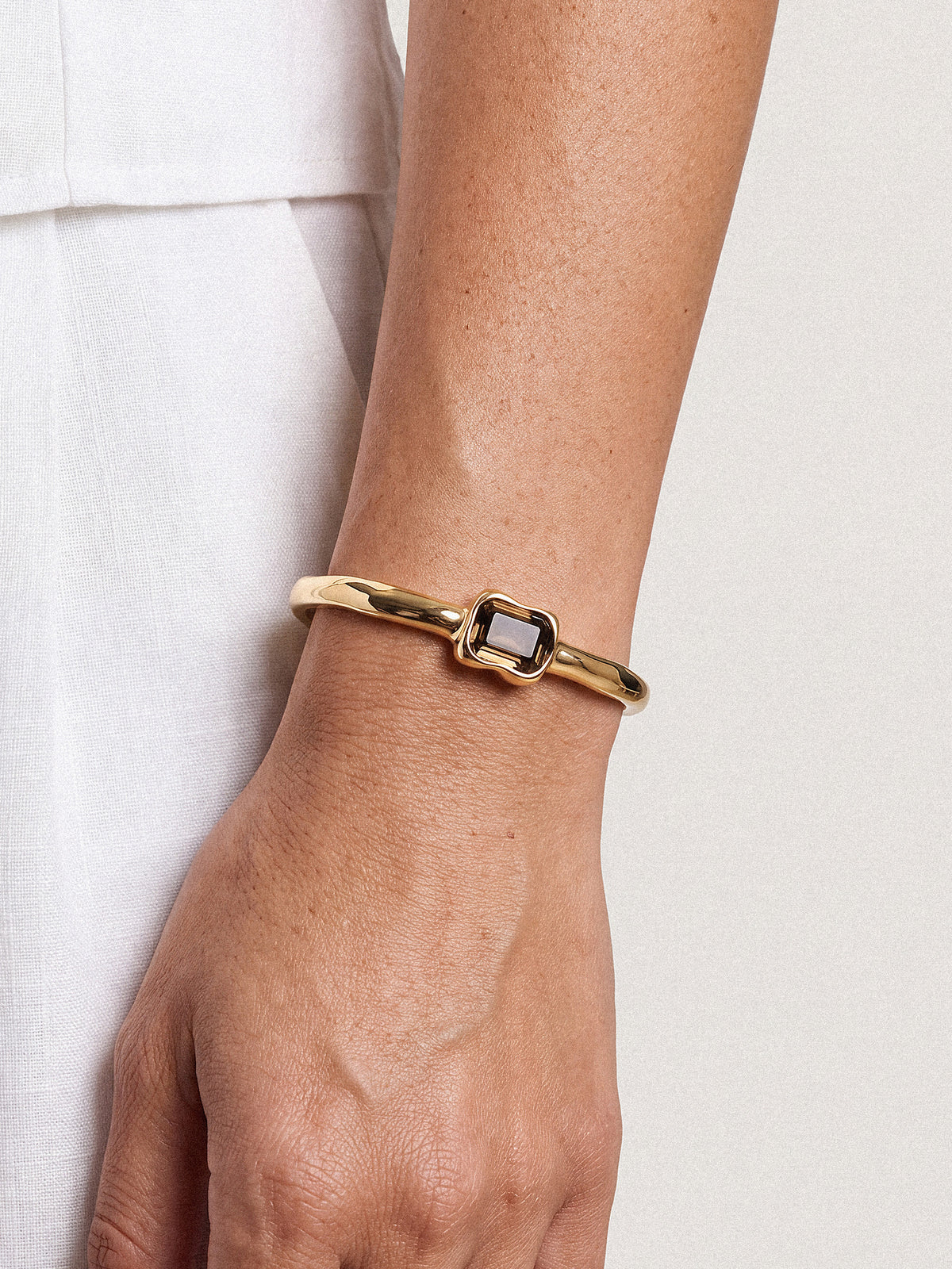A gold bangle bracelet with a central black square bezel, shown worn on a person's wrist against a light-colored background.