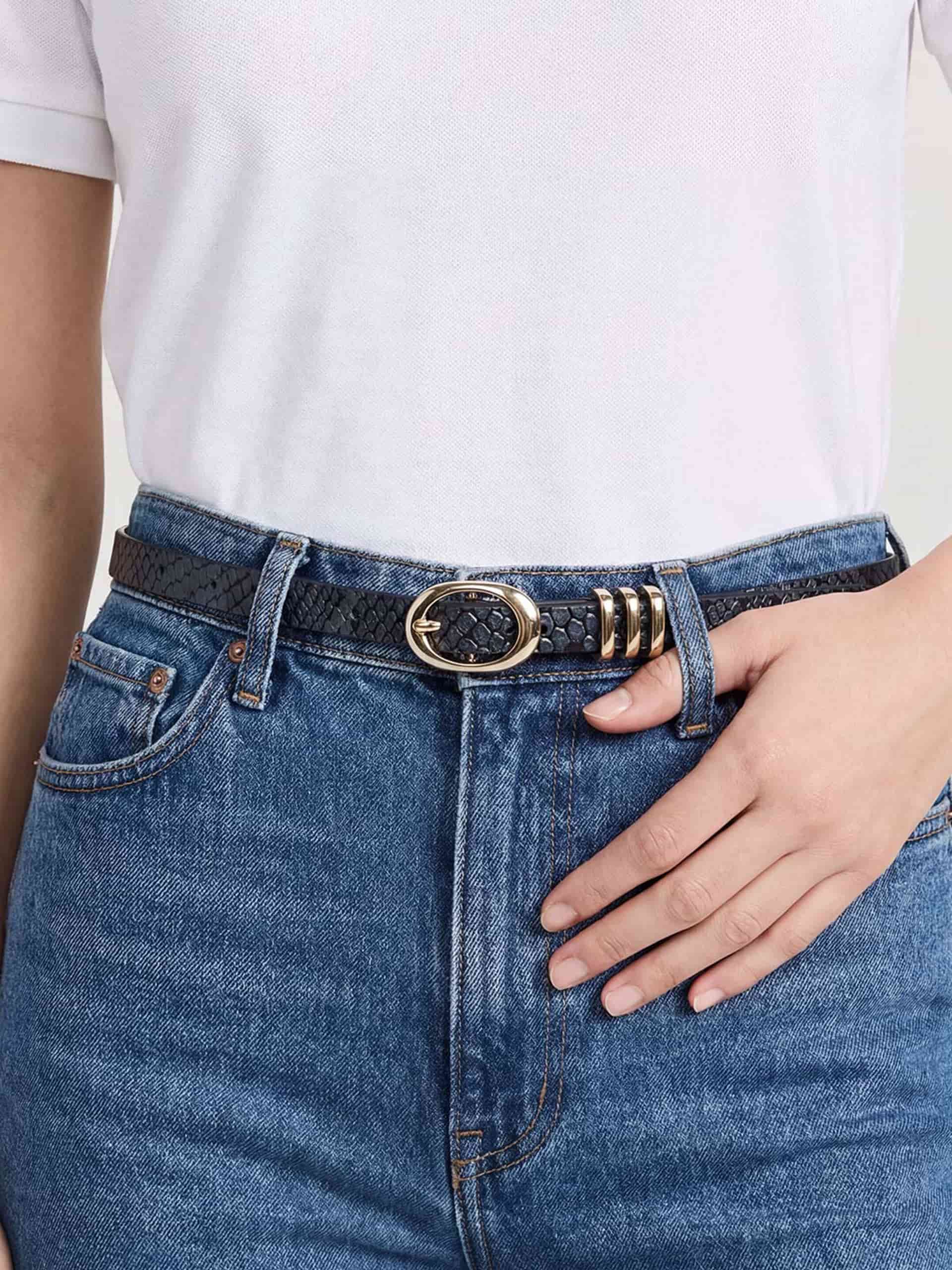 Close-up of grey belt with oval buckle styled on high-waisted blue jeans and white top