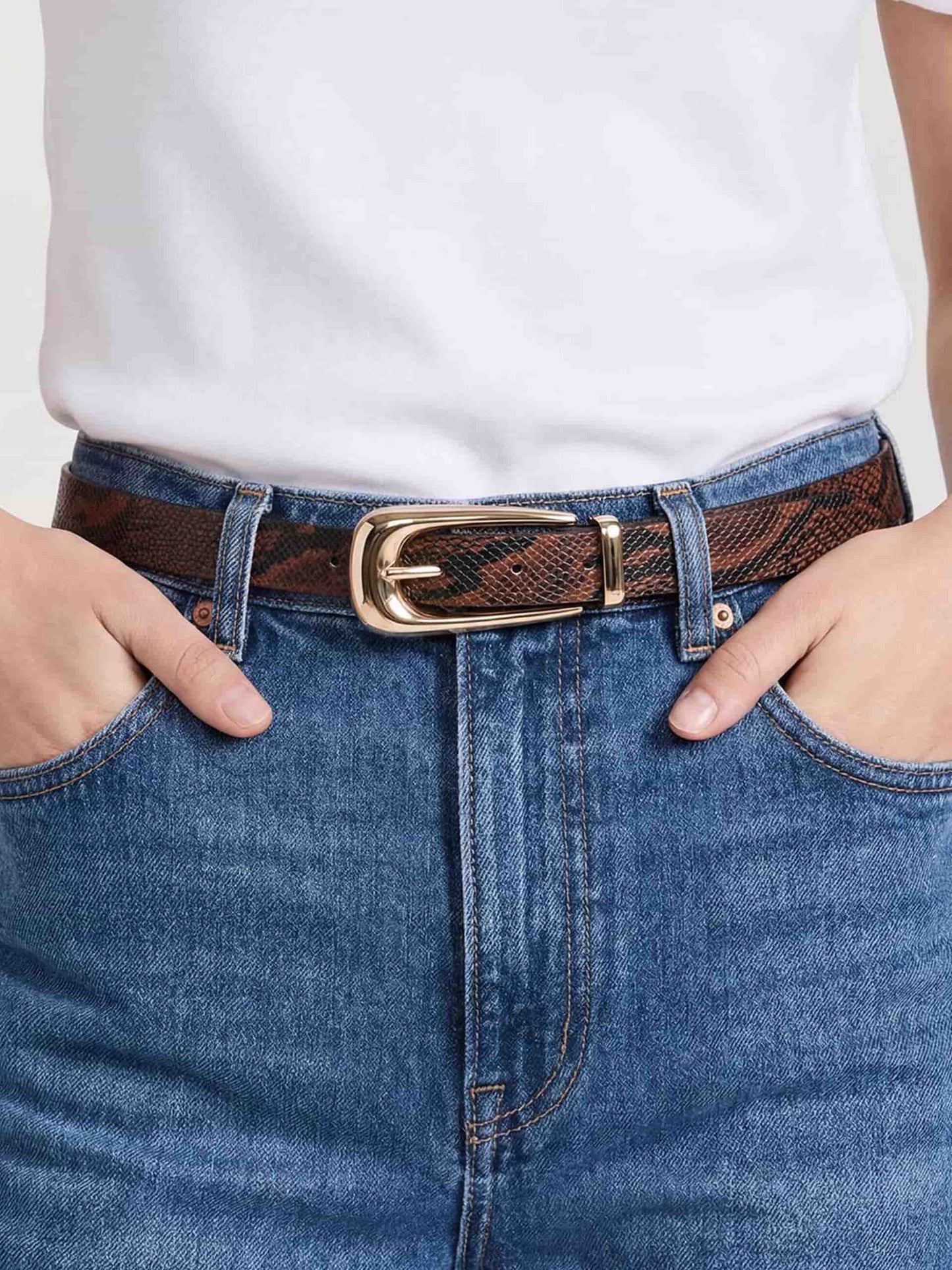 Close-up of brown snakeskin-textured belt with gold buckle, styled with white top and denim jeans.