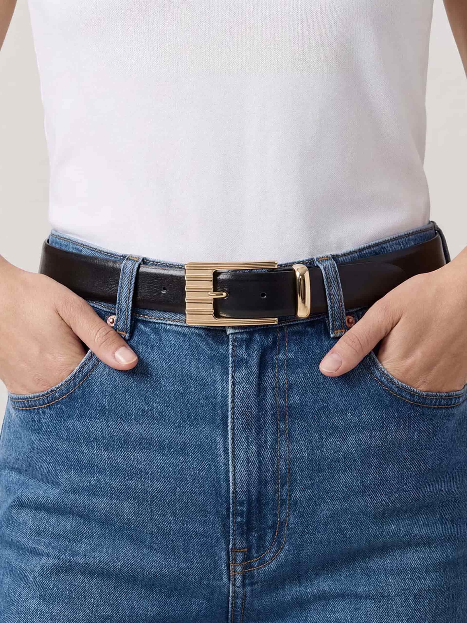 Close-up of black leather belt with wide gold buckle, styled with white shirt and blue jeans.