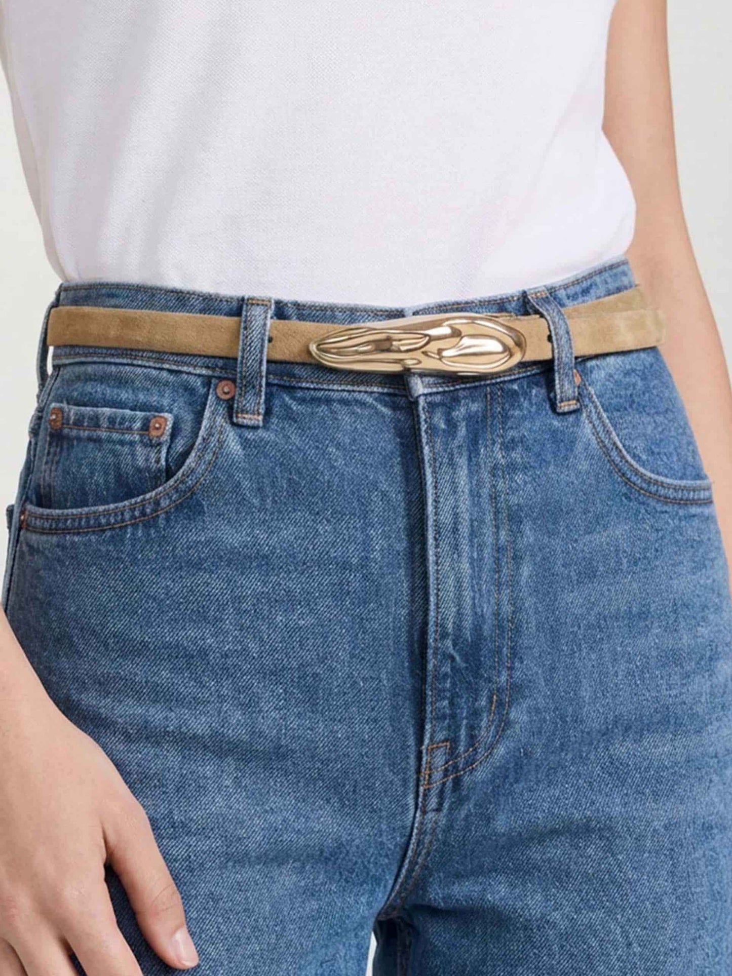 Skinny gold belt with swirl buckle styled with jeans and white top.