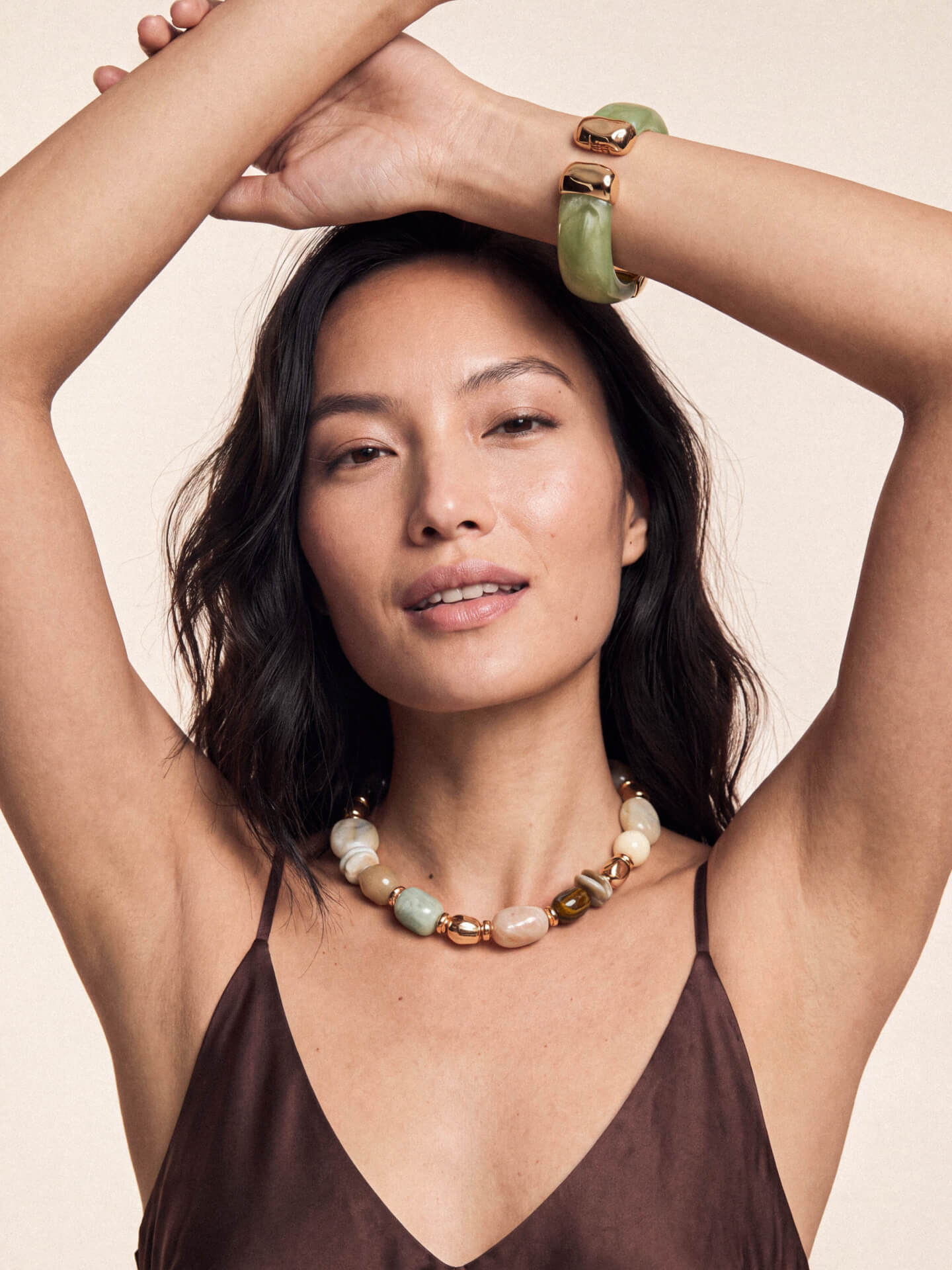 Model posing with arms raised, showcasing beaded necklace and matching bracelet