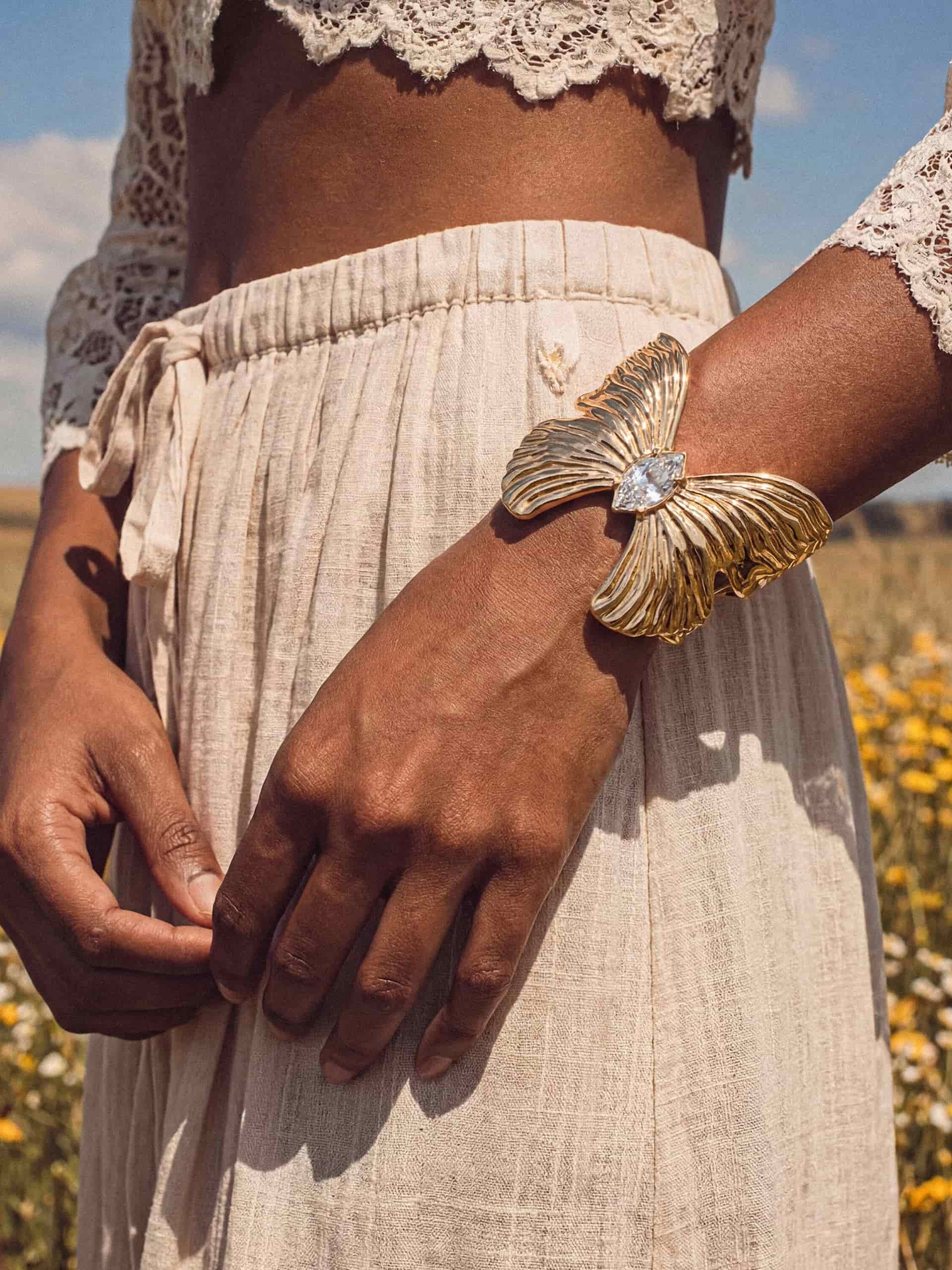 Woman in white lace crop top with gold butterfly bracelet