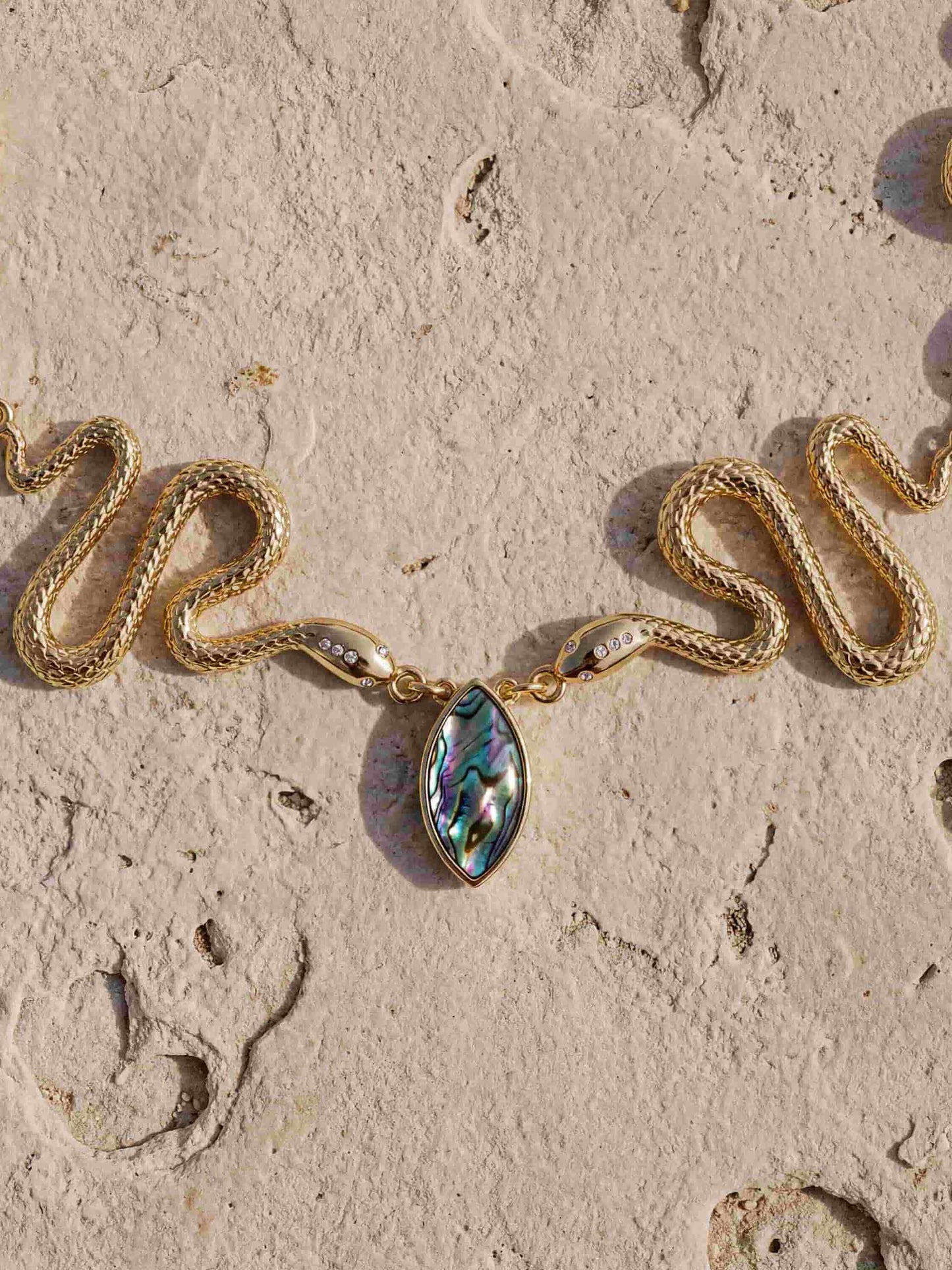 Close-up of gold necklace with sculptural pendant and abalone stone accent.