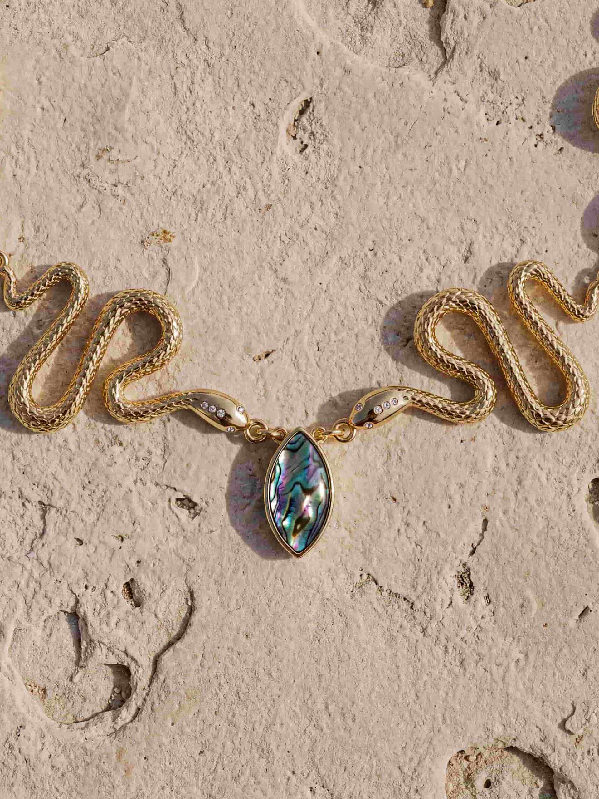 Close-up of gold necklace with sculptural pendant and abalone stone accent.
