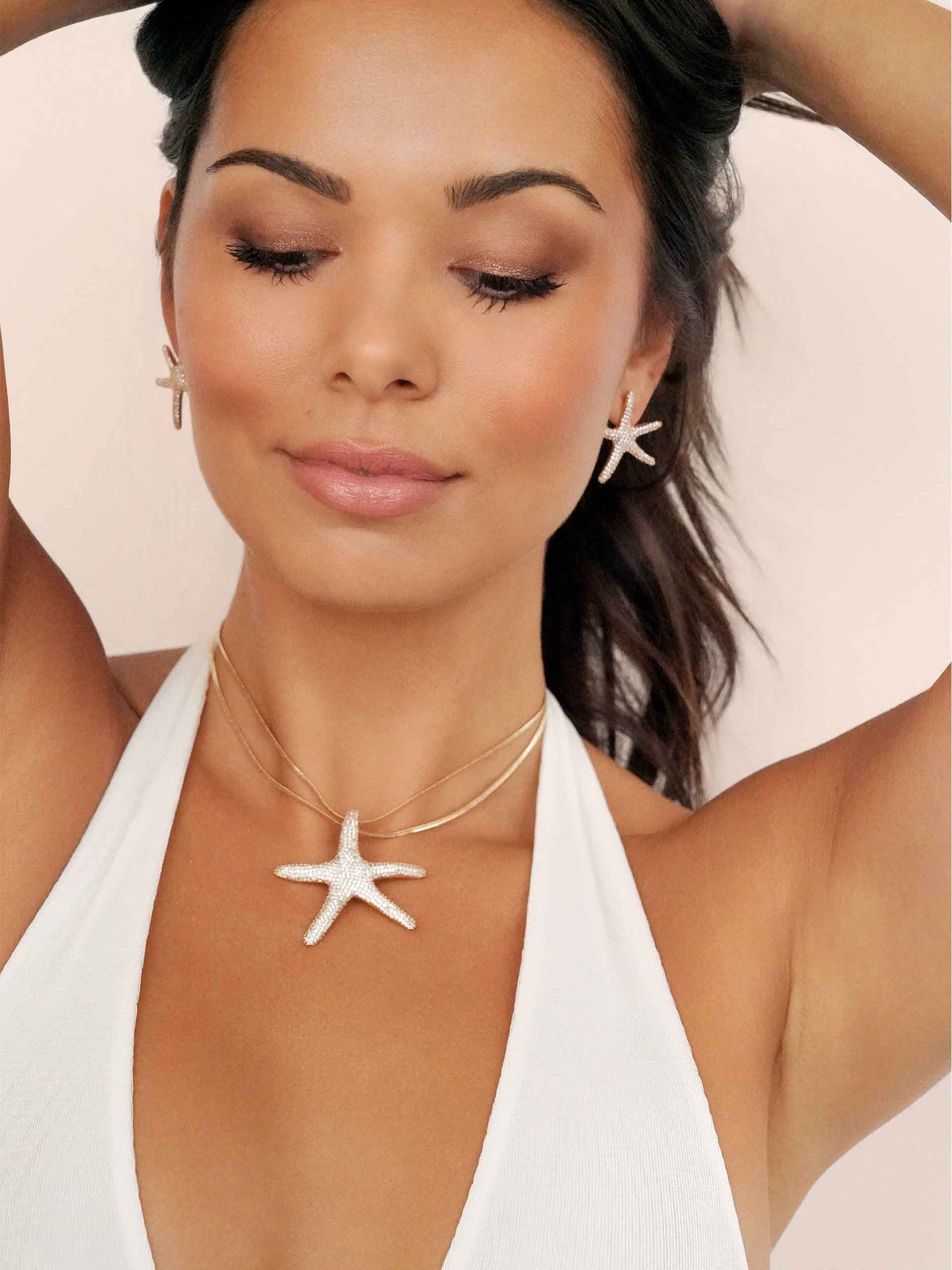 Woman wearing a starfish necklace and earrings on a light pink background
