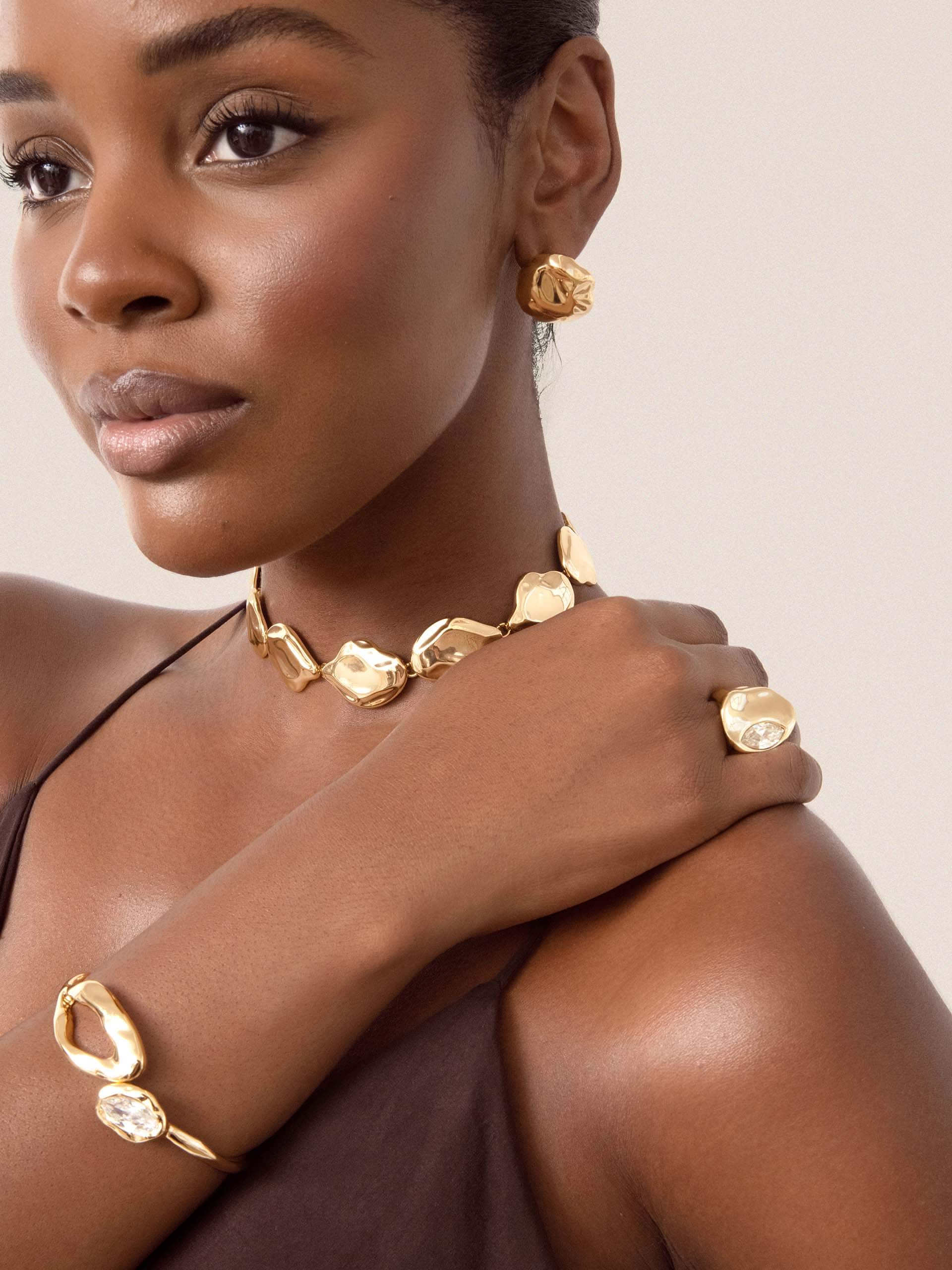 Woman model wearing gold jewelry including earrings, necklace, and bracelet on a beige background 3