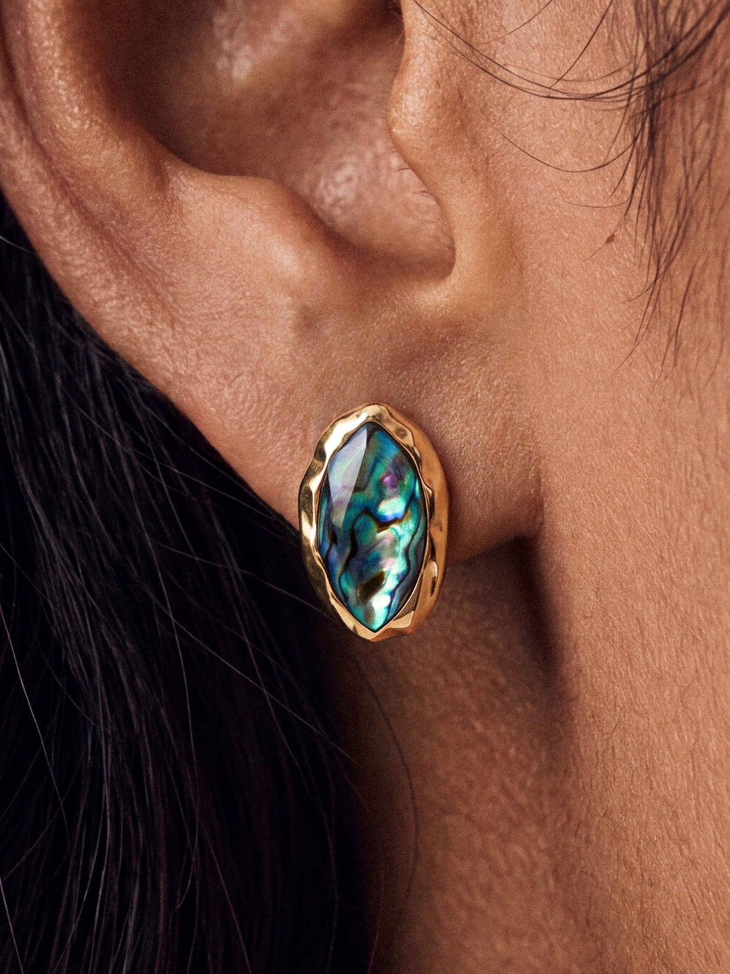 Model wearing a gold-framed abalone luxe shell earring with vivid iridescent blues and greens, conveying elegance and style.