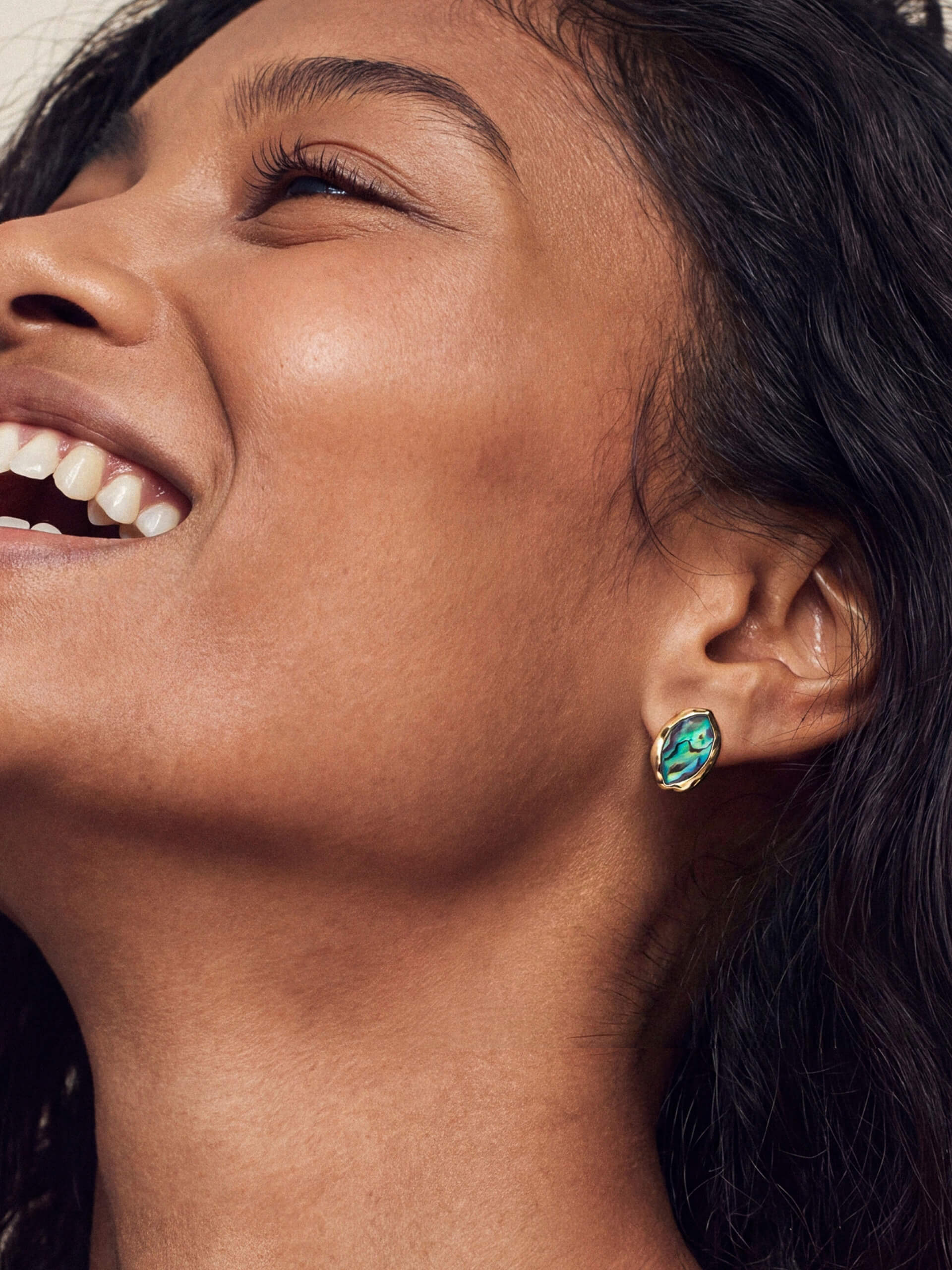 Model wearing a gold-framed abalone luxe shell earring with vivid iridescent blues and greens, conveying elegance and style.