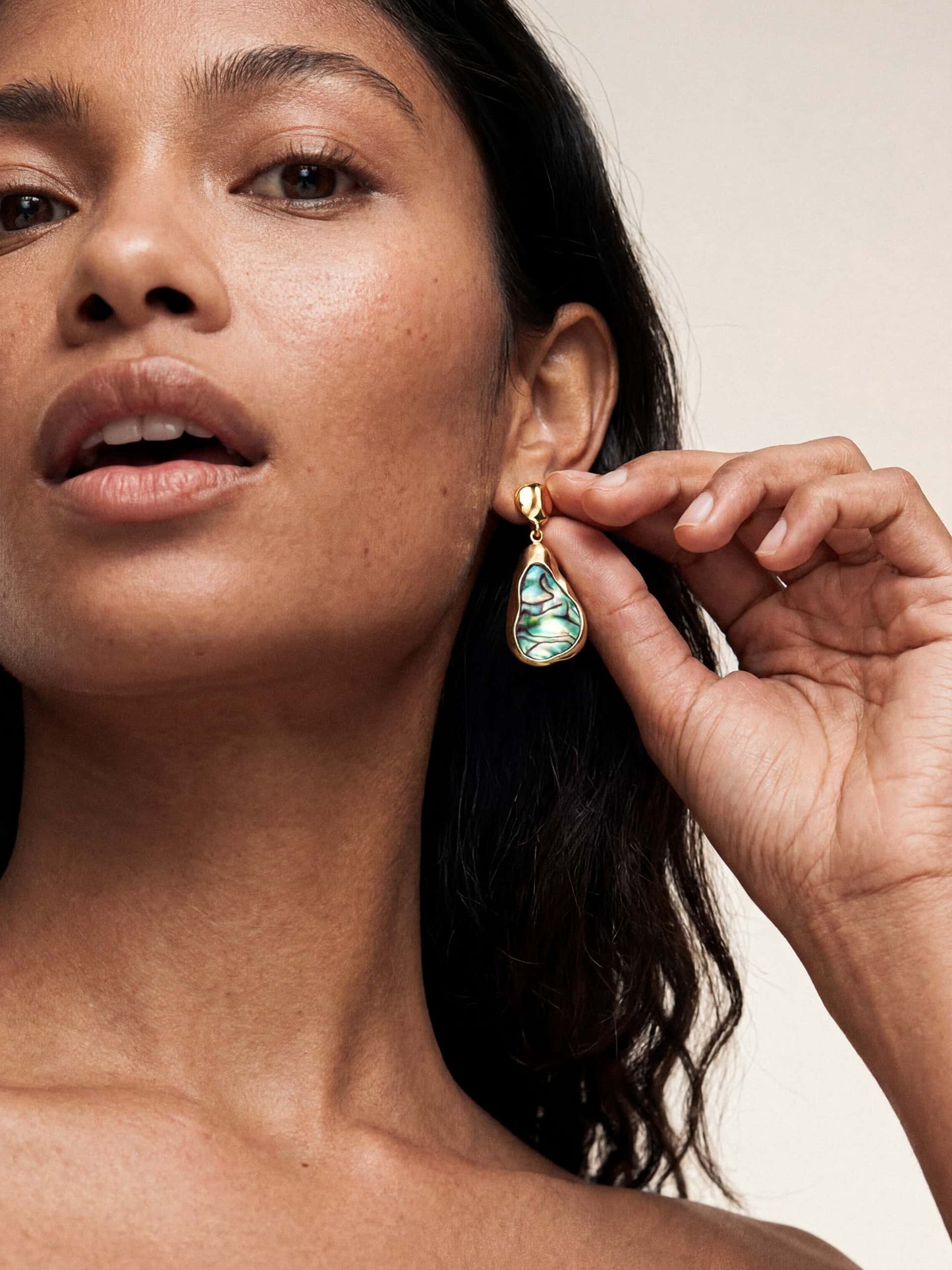 Woman holds a dangling abalone earring near her ear
