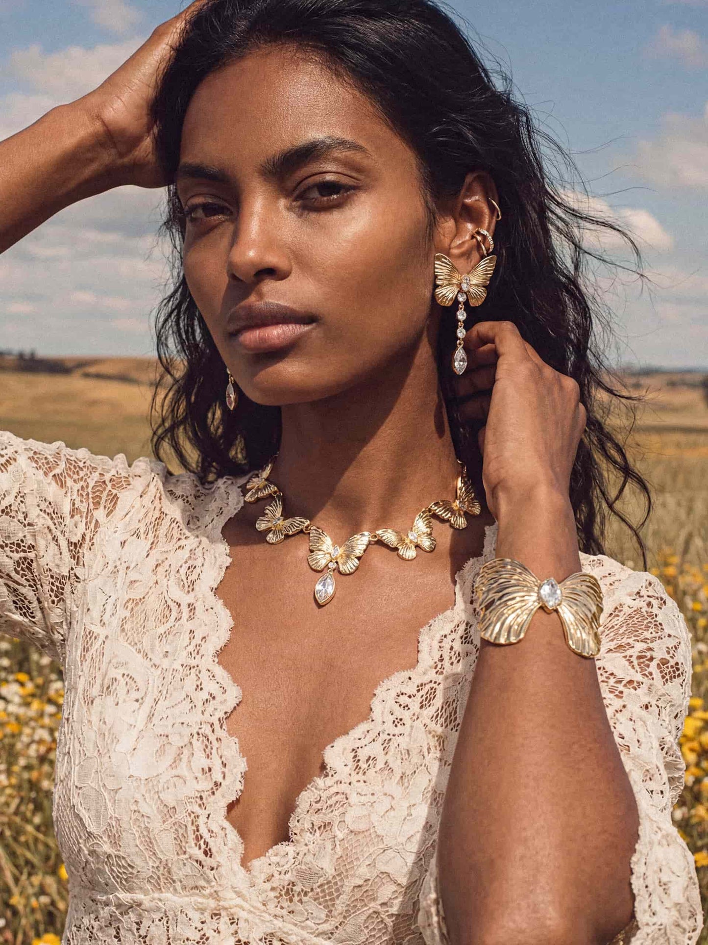 Gold butterfly and crystal necklace, earrings and cuff on woman in white lace dress