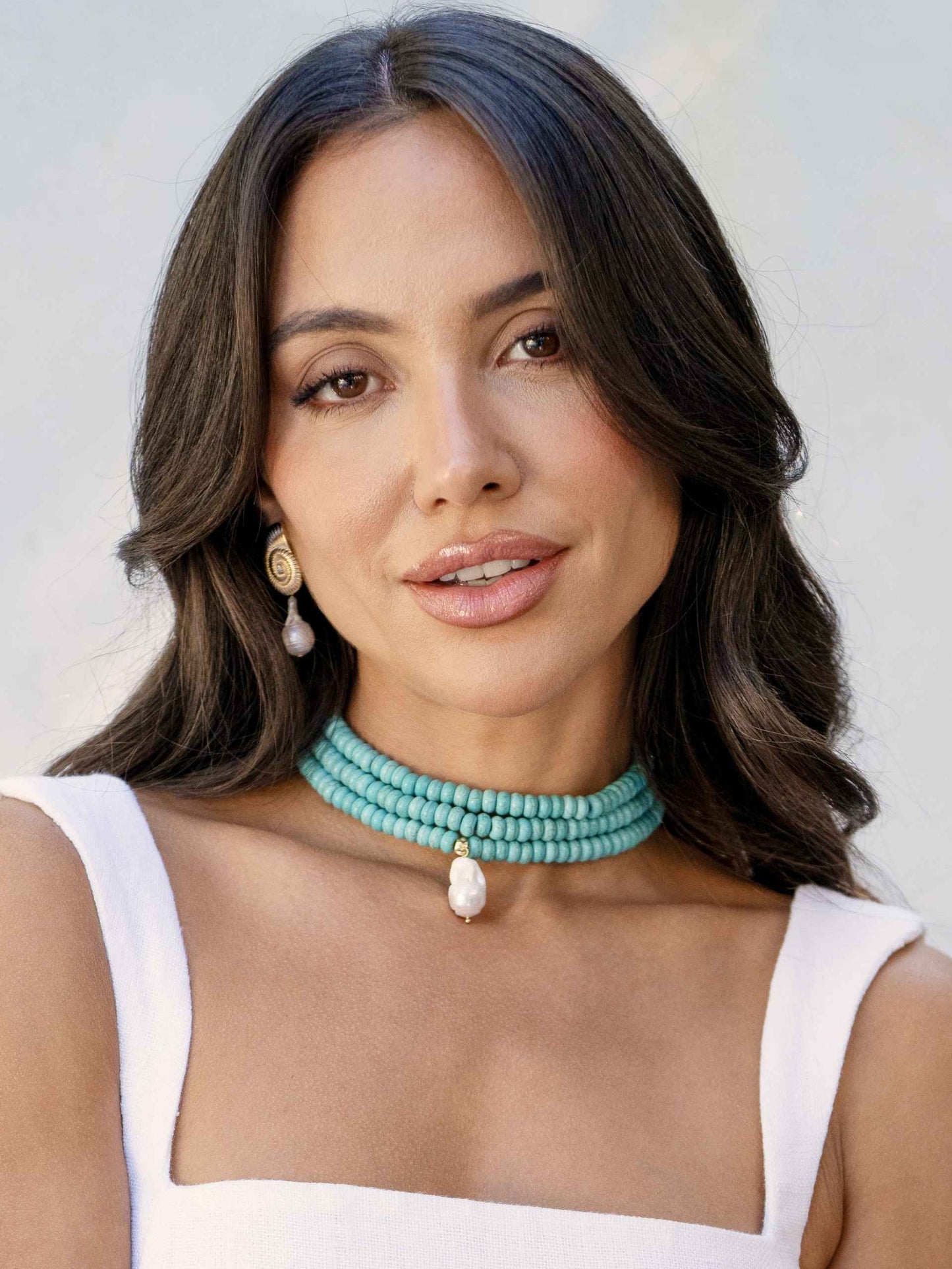 Woman wearing a turquoise beaded necklace against a neutral background