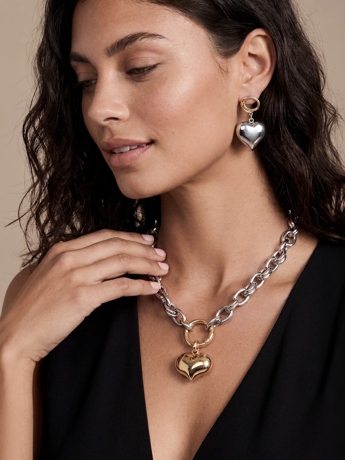 Model wearing metallic heart-shaped earrings and a chunky chain necklace with a gold heart pendant.