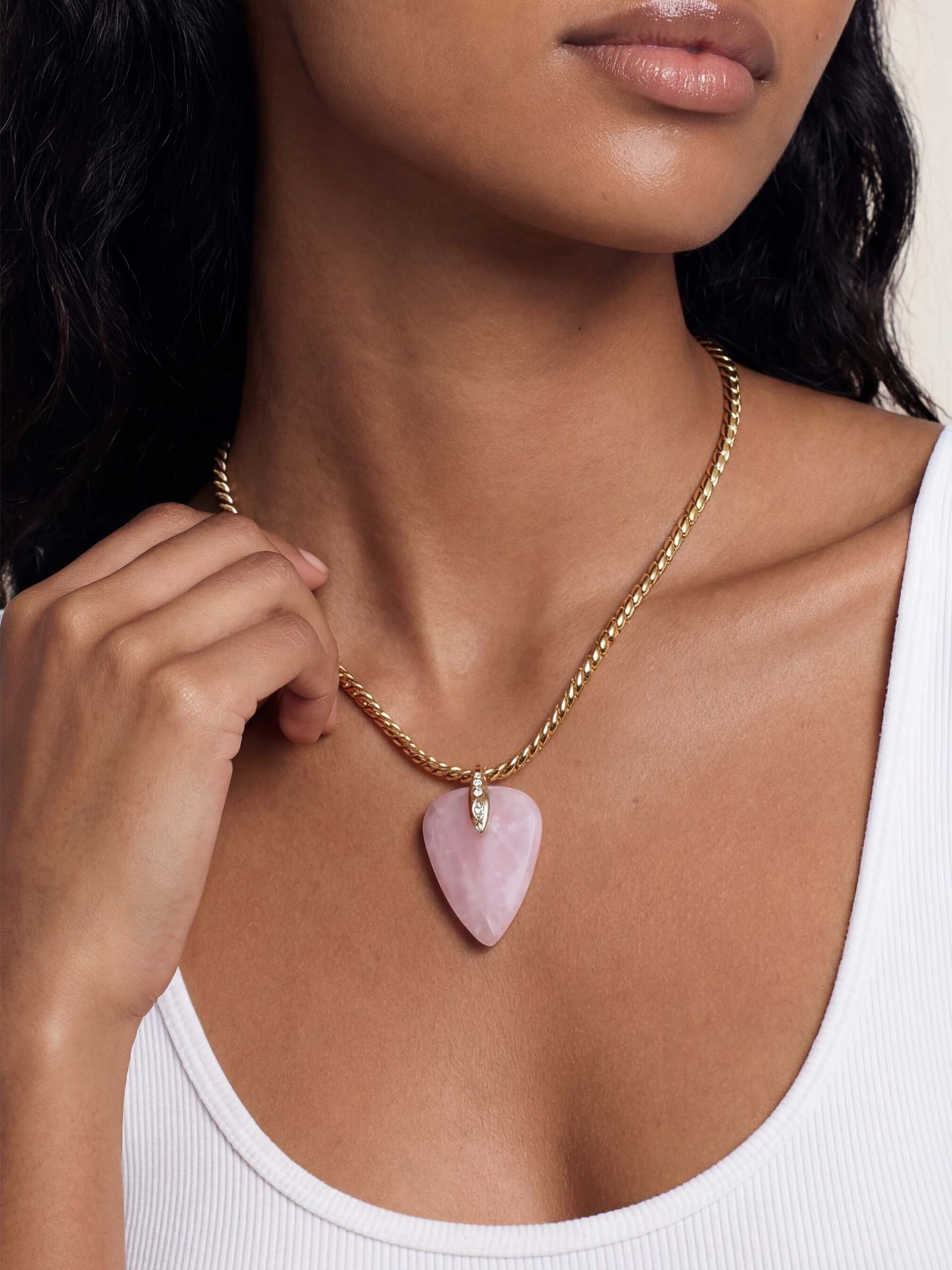 A gold chain necklace with a pink heart-shaped pendant is worn around a woman's neck. The pendant has a small diamond accent on top, set against a bare skin backdrop, exuding elegance.