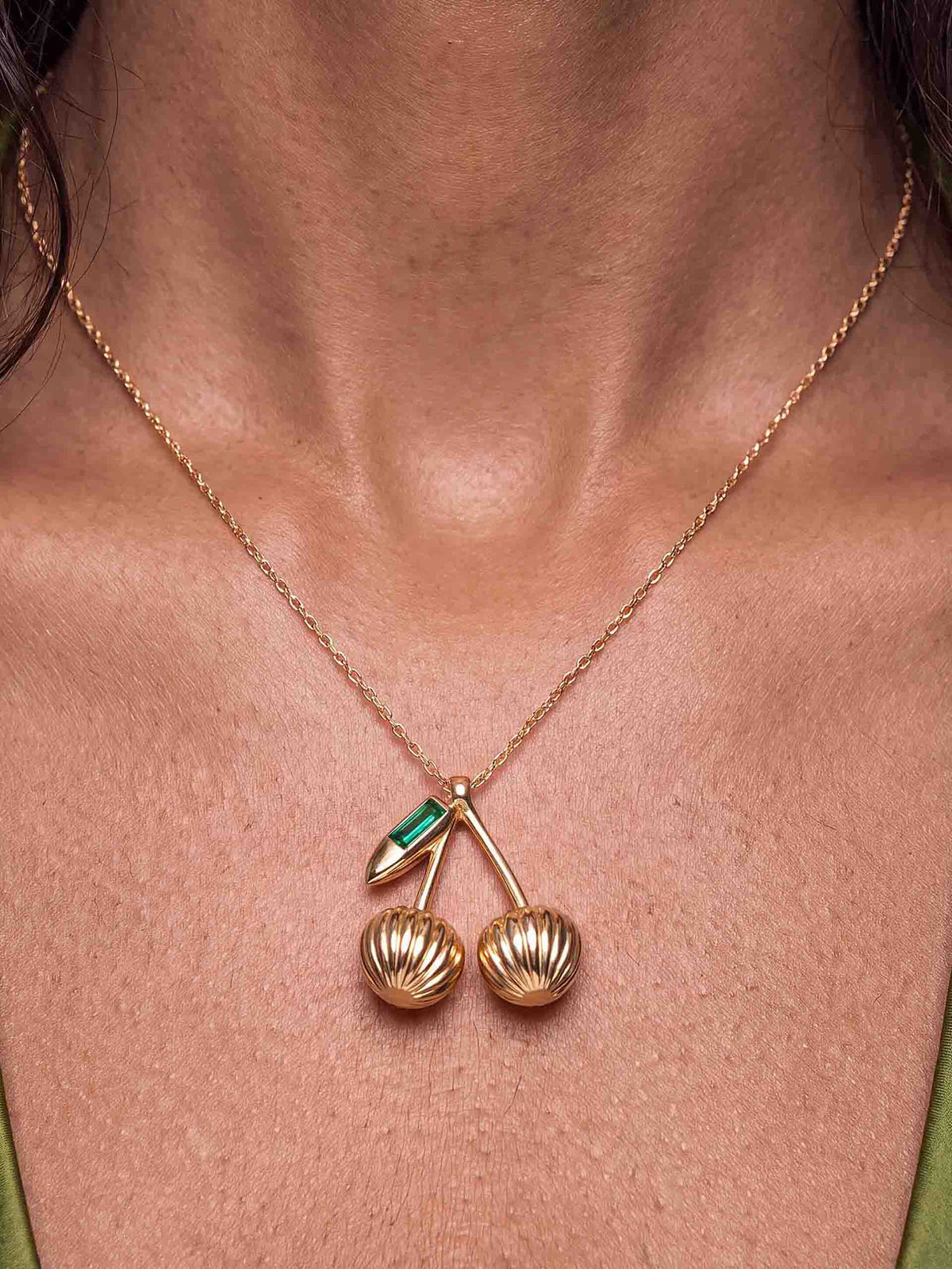 Close-up of a woman in an olive satin V-neck top, wearing a fine gold necklace.