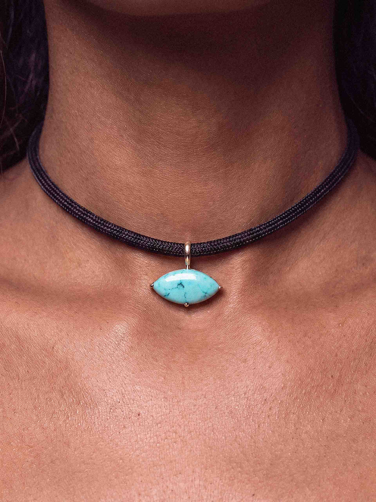 Close-up of a person wearing a black braided choker with a bright turquoise, marbled stone pendant at the center; simple, understated jewelry.