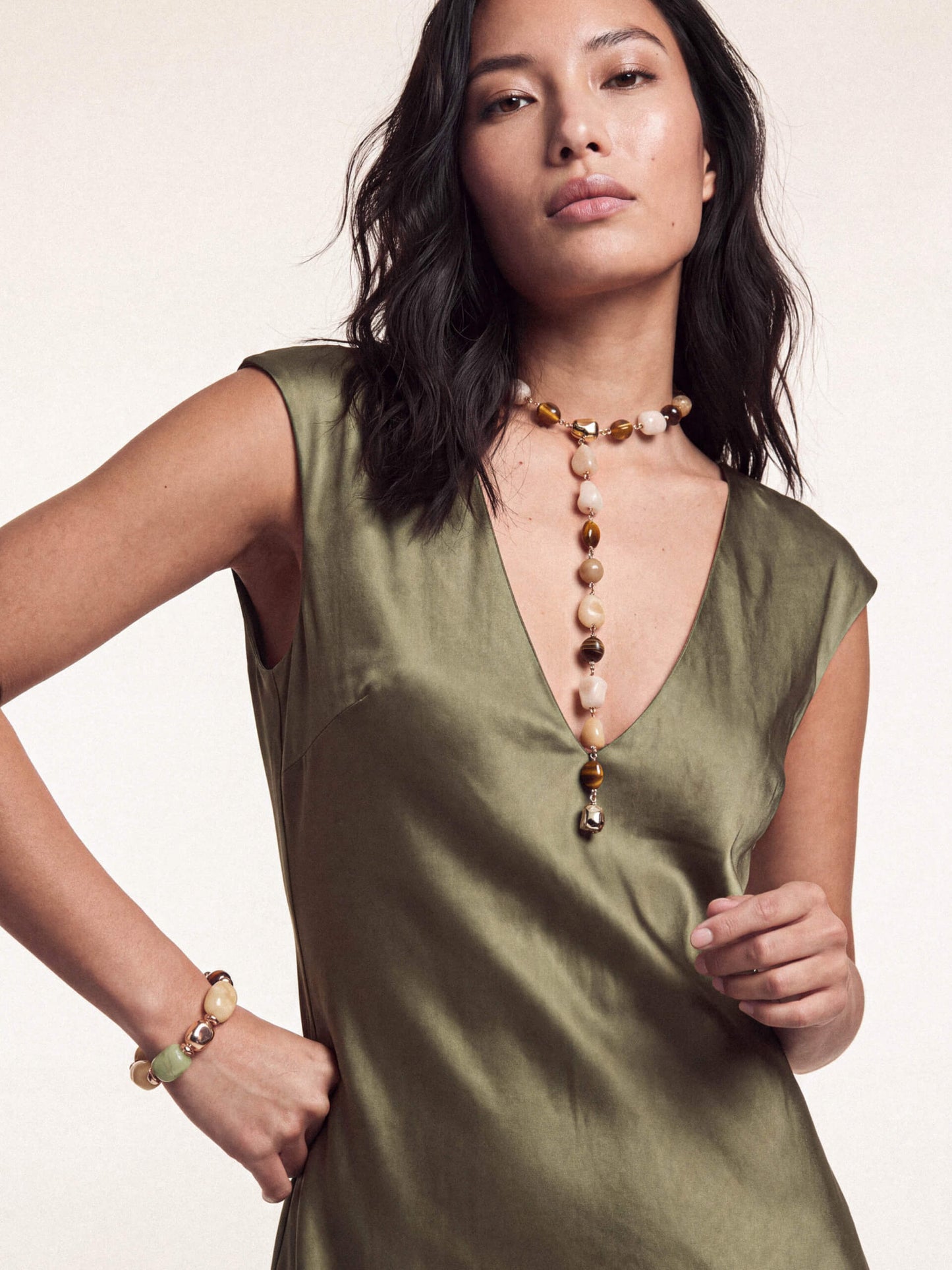 Model in green satin dress featuring long pendant necklace