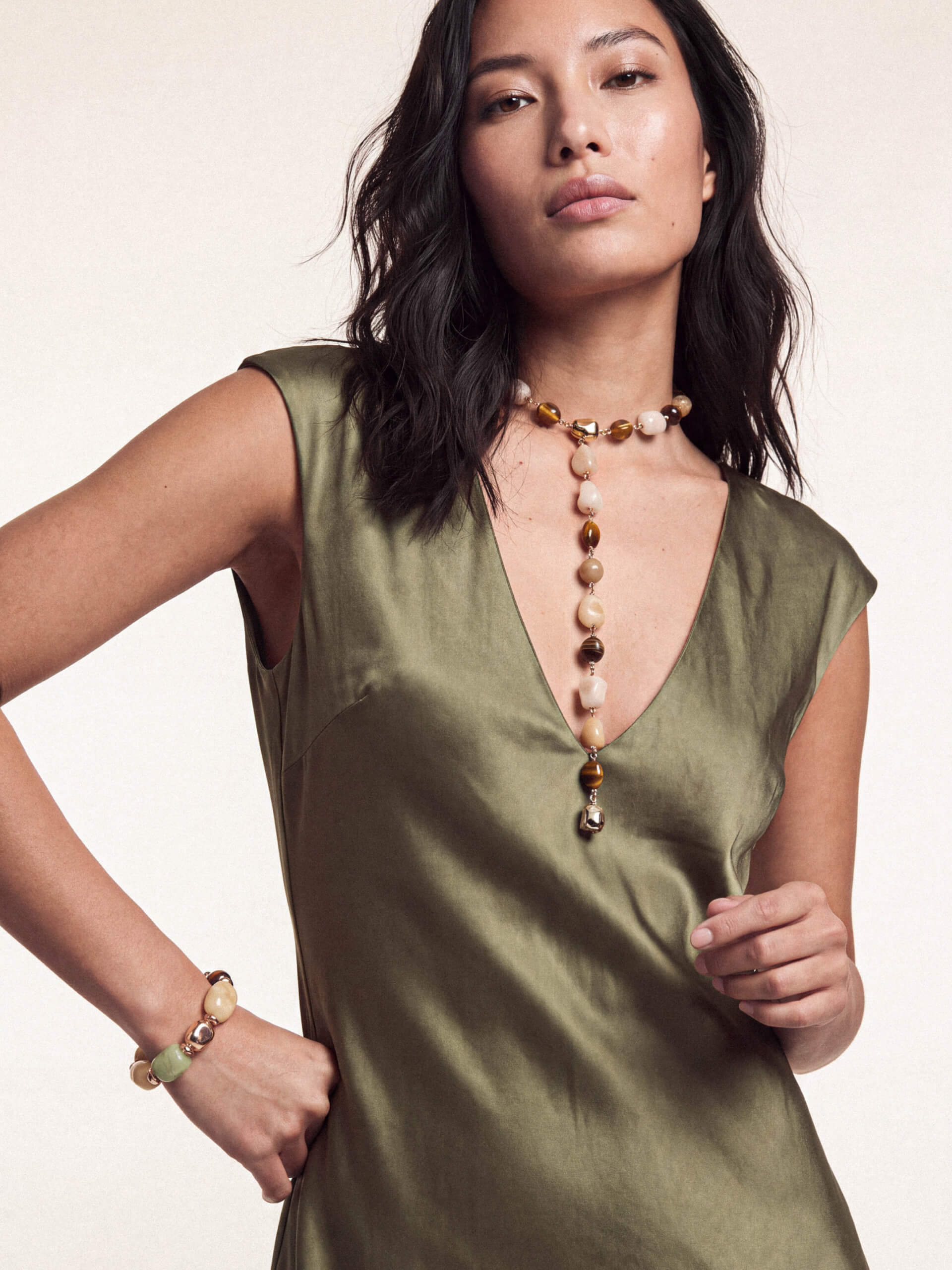 Model in green satin dress featuring long pendant necklace