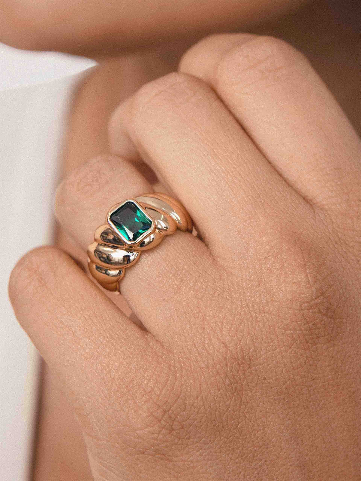 A close-up of a hand wearing a gold ring with a square-cut green gemstone.