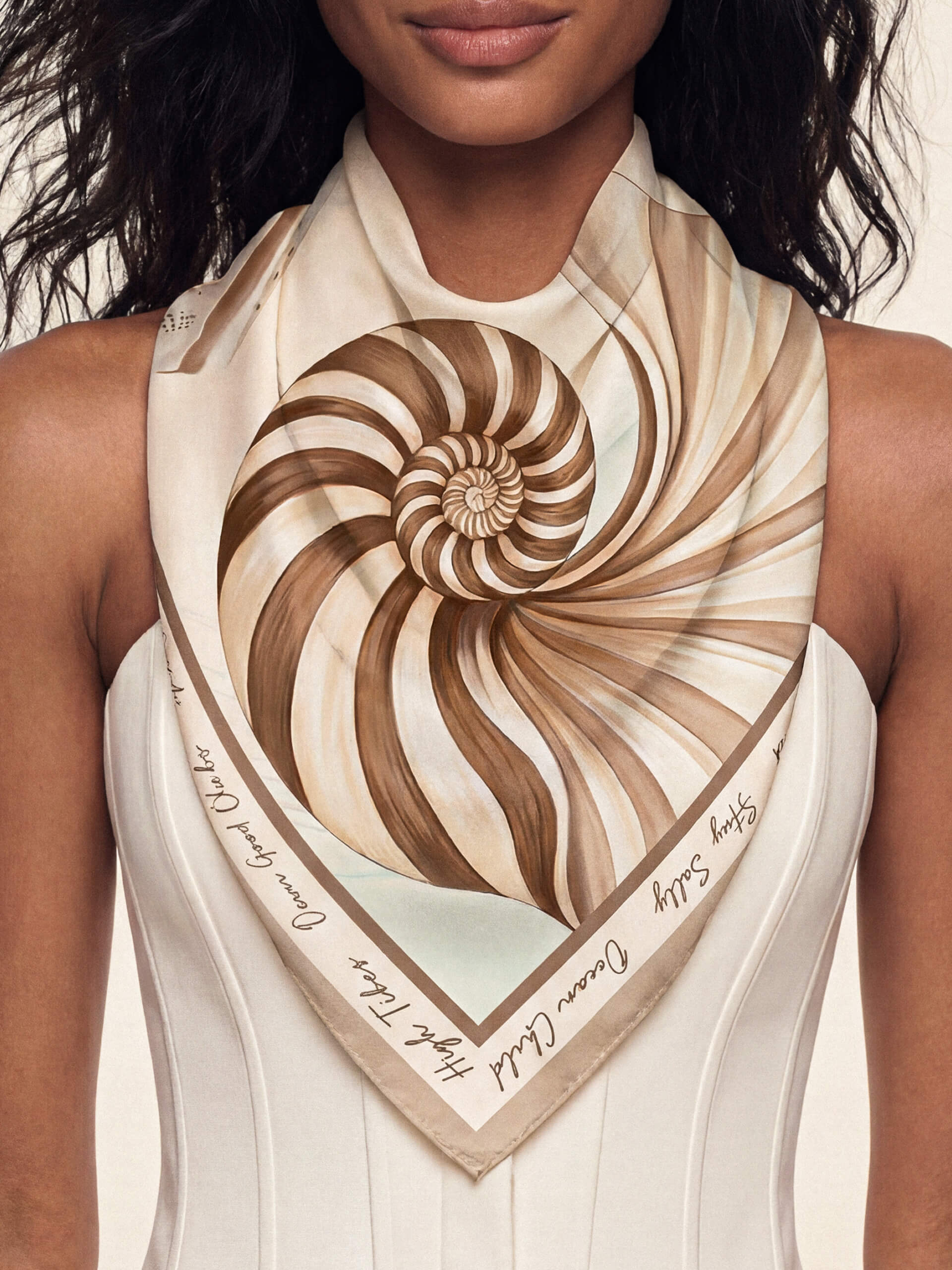 A woman wearing a Coastal Sea Shell Scarf with a spiral seashell design in brown and cream hues. 