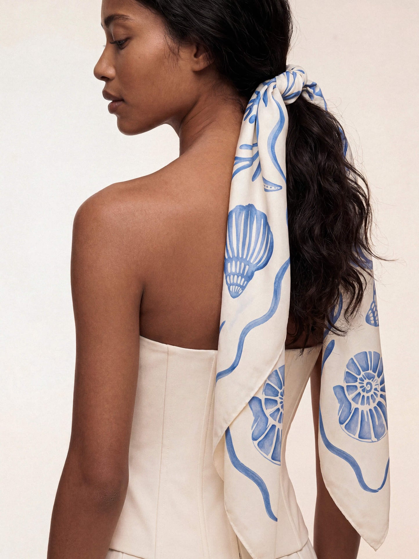 A woman wearing a white scarf with blue shell patterns tied around her ponytail.