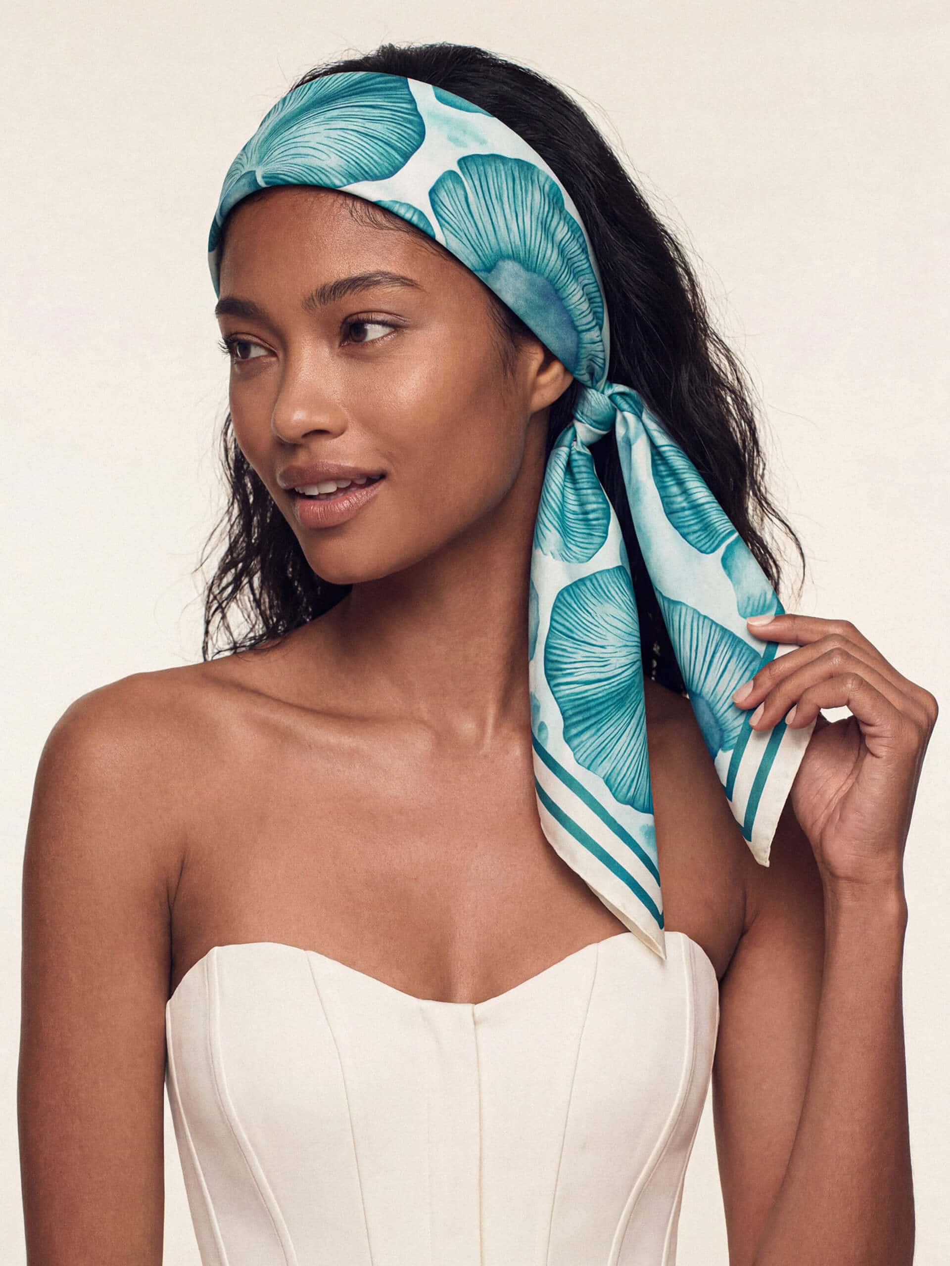 A model with long hair wears a teal floral headscarf tied in a bow