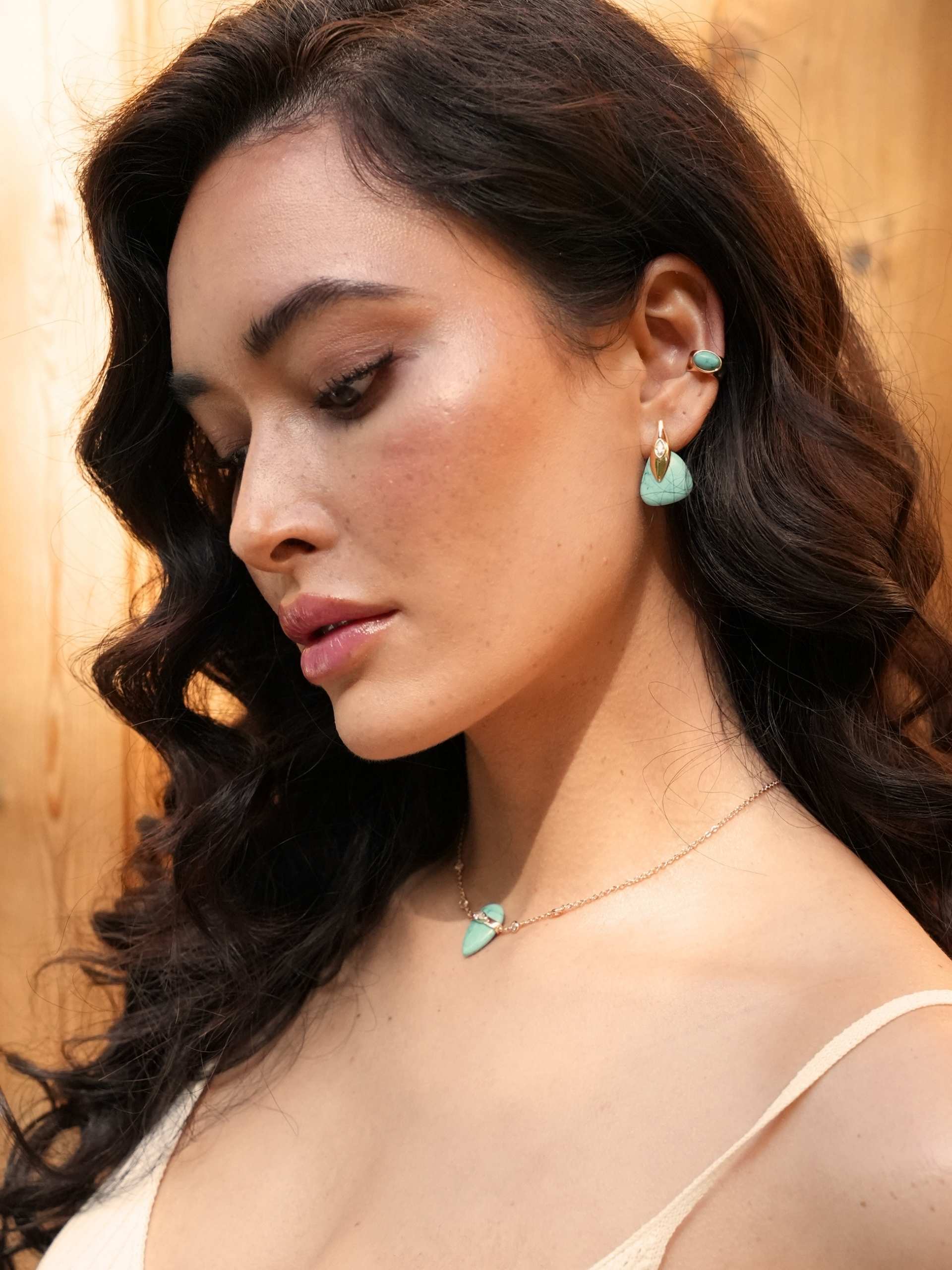 Close-up of a woman wearing turquoise earrings and necklace against a warm-toned background