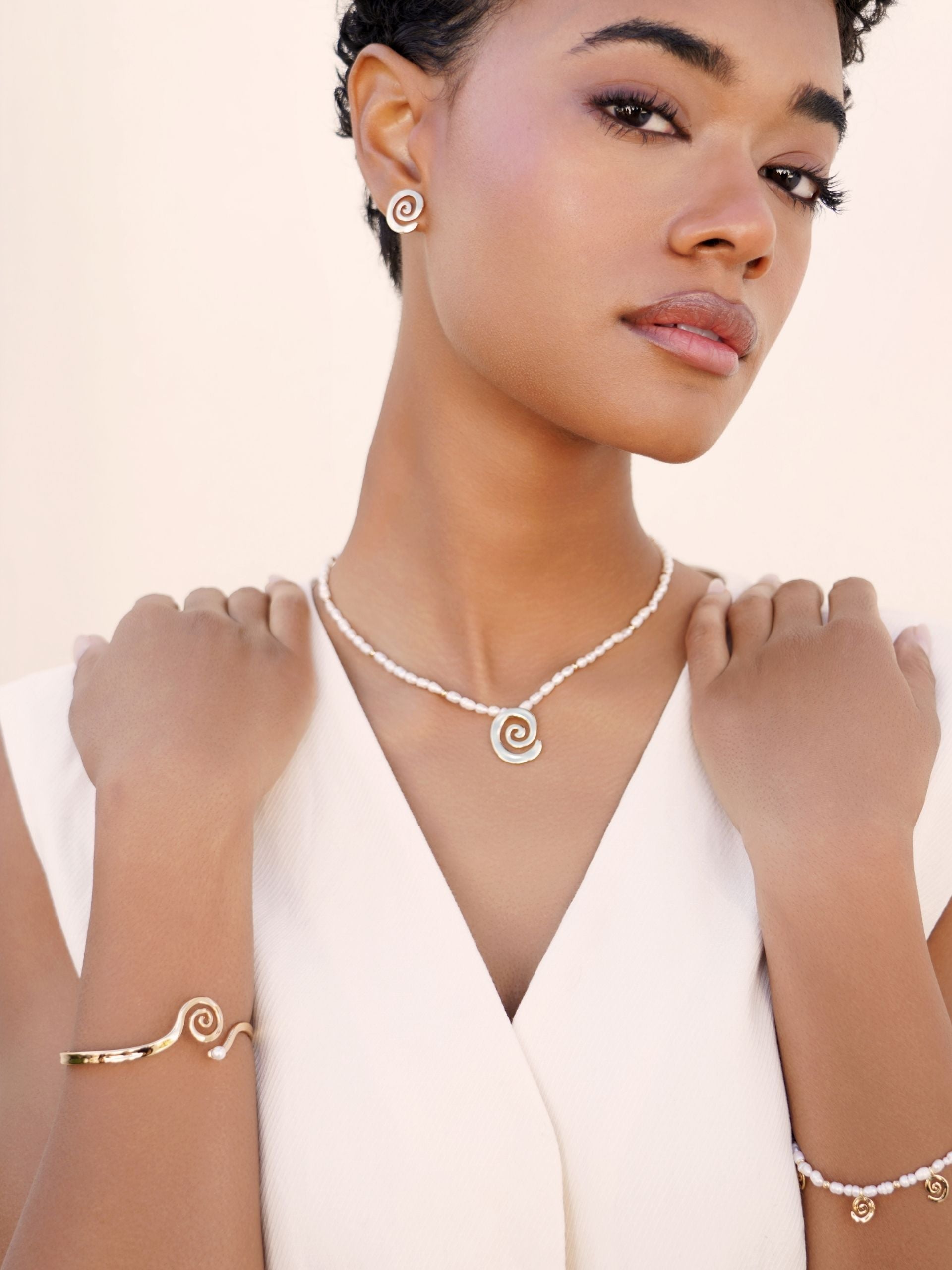 Woman wearing a pearl necklace, earrings, and bracelet on a plain background