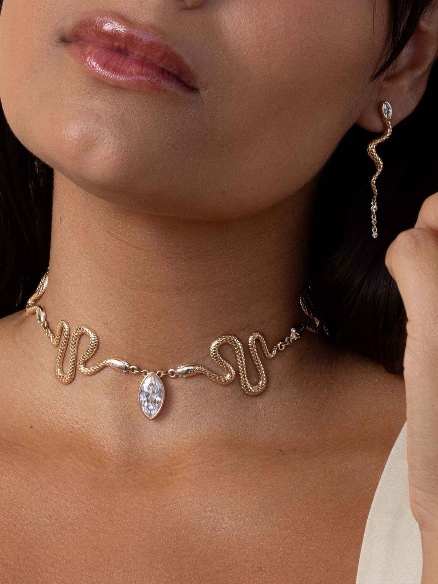 Close-up of a person wearing a gold necklace with a clear gemstone and matching earrings.