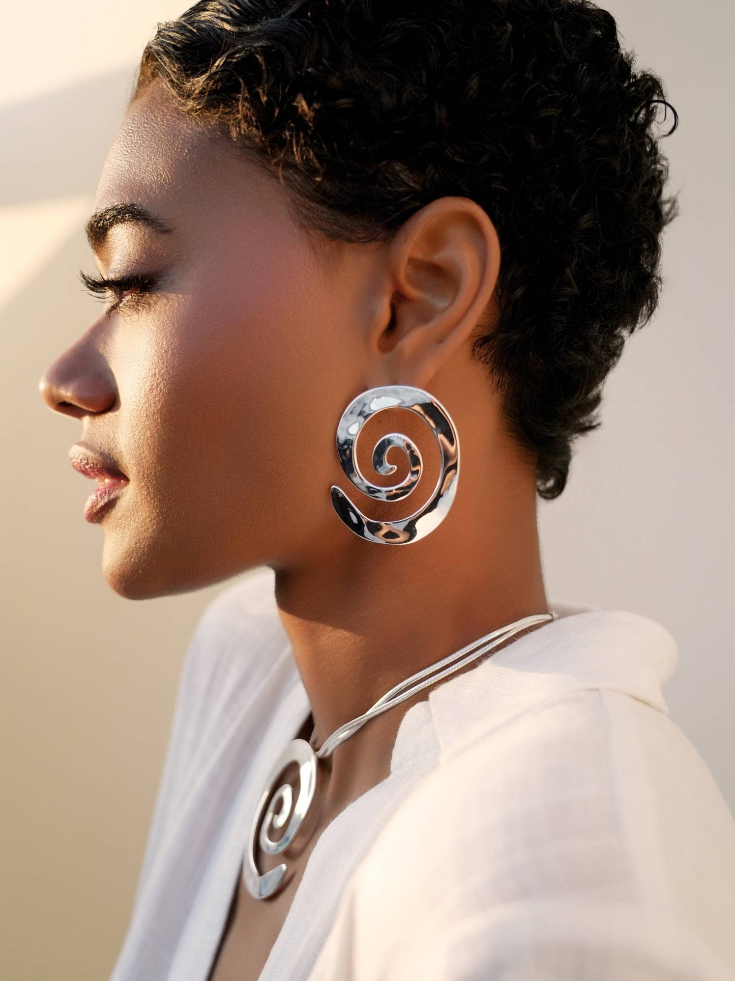 Woman wearing silver spiral earrings and necklace against a neutral background