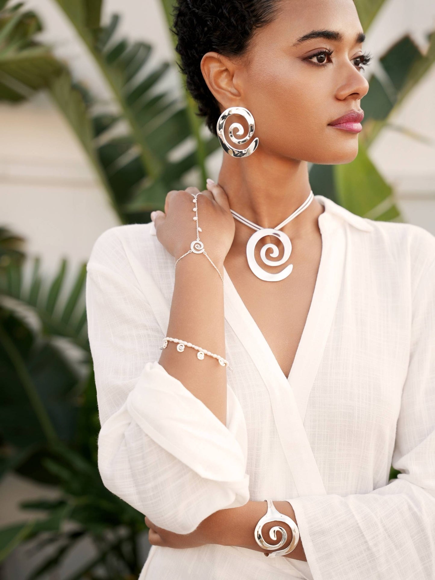 Woman wearing spiral jewelry set with a white top against a blurred green background
