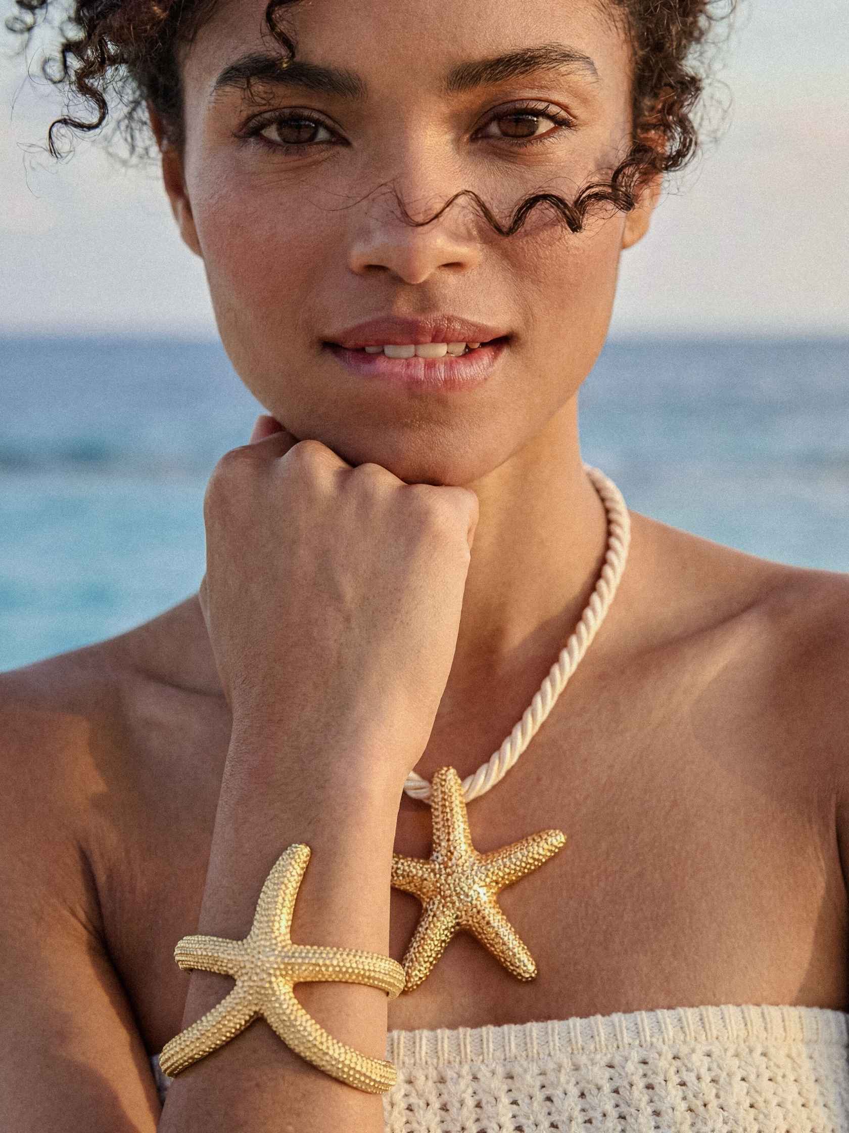 Woman wearing a gold starfish bracelet and necklace with ocean in the background