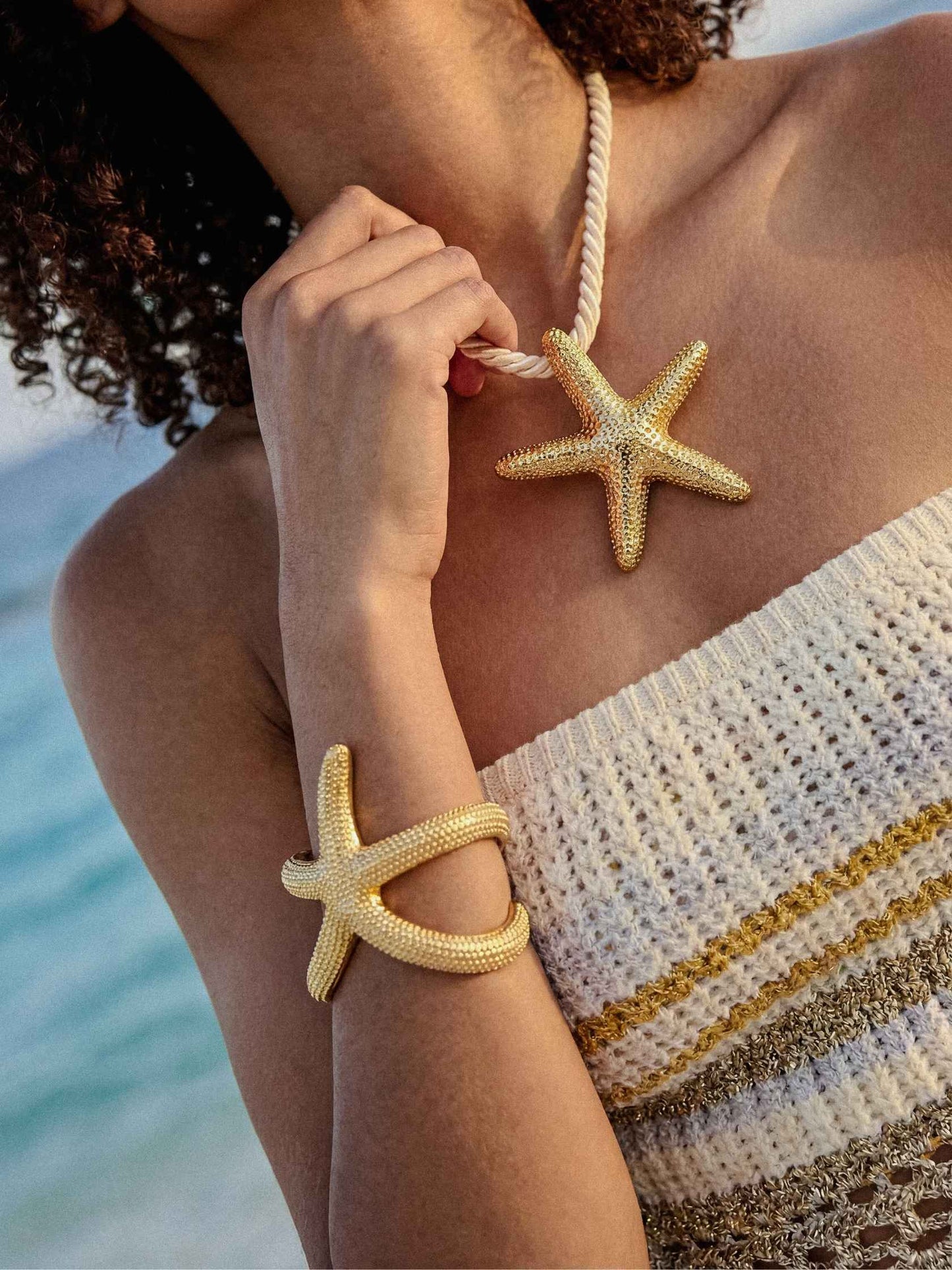 Woman wearing a starfish-shaped necklace and bracelet with a blurred beach background