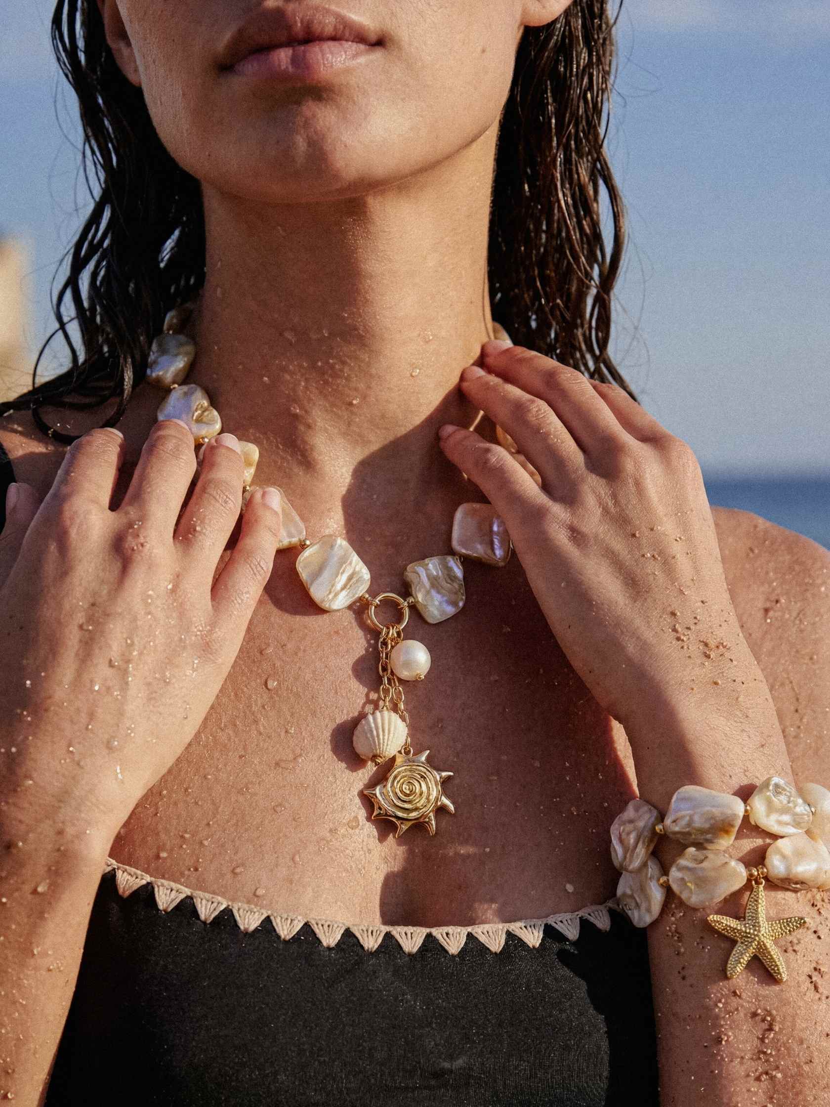 Person wearing a necklace with shell and starfish charms on a beach.