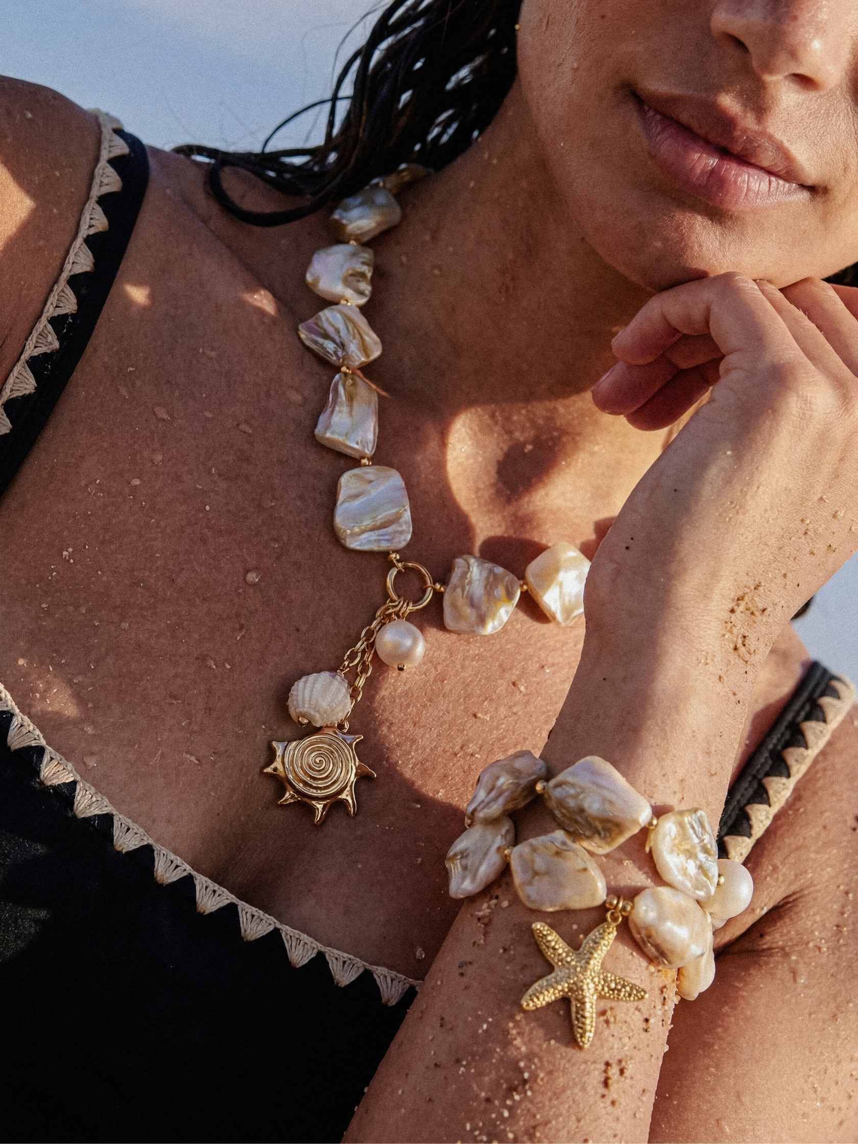 Close-up of a person wearing a shell necklace and bracelet with a sun and starfish charm.